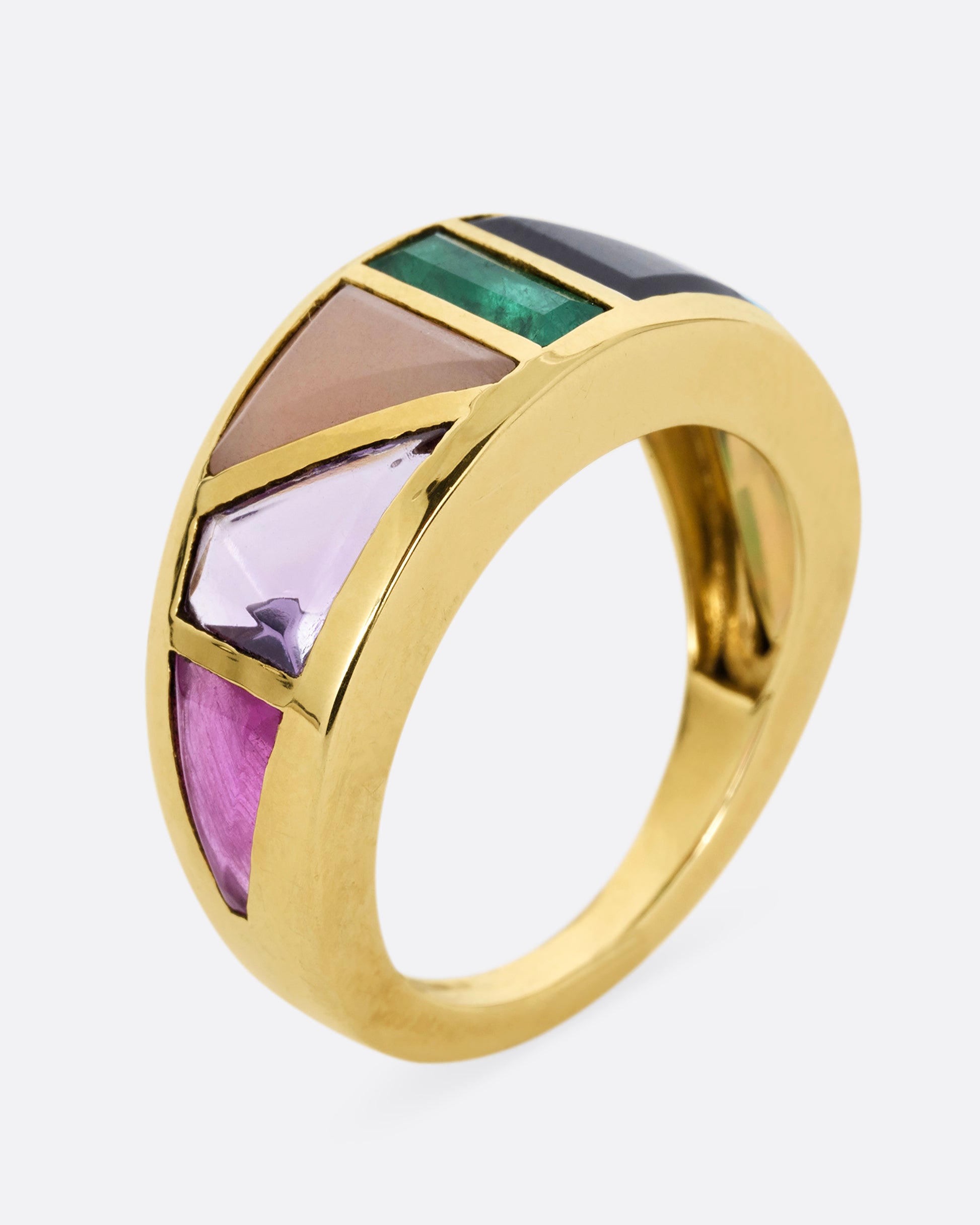 A yellow gold band with an array of gemstones in angular shapes. Shown standing up from the side.