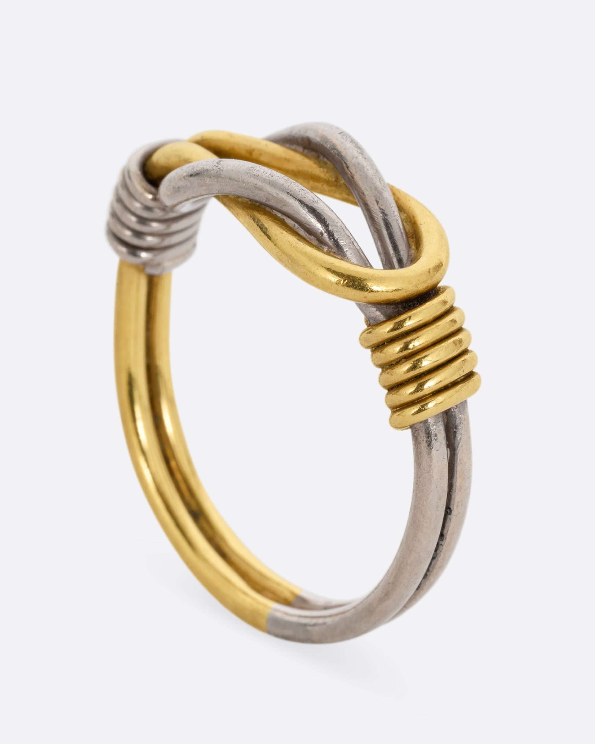 A white and yellow gold infinity knot ring. Shown standing up from the side.