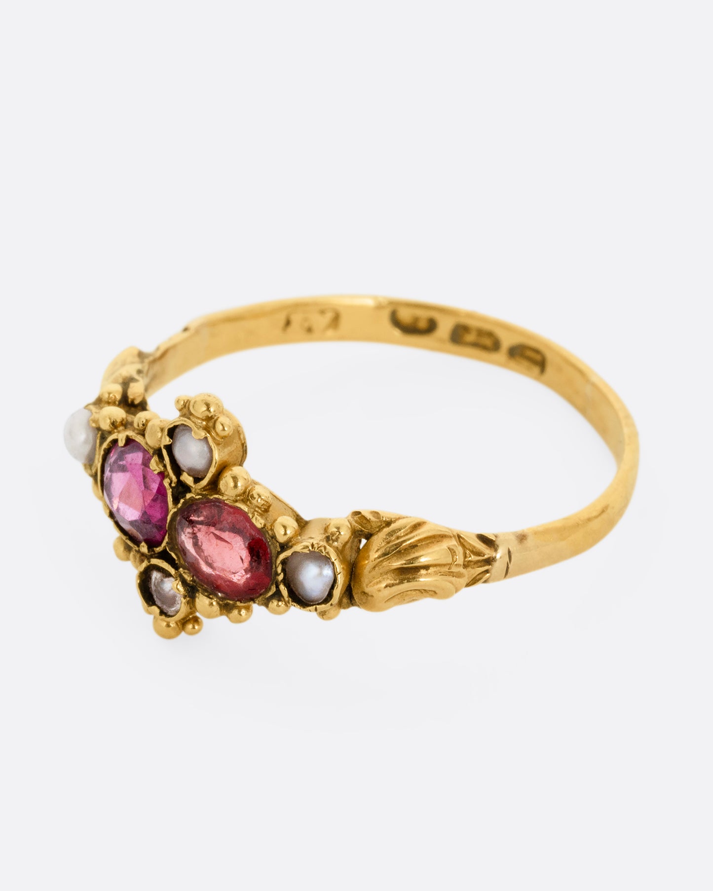 A yellow gold ring with garnets and seed pearls. Shown from the side.