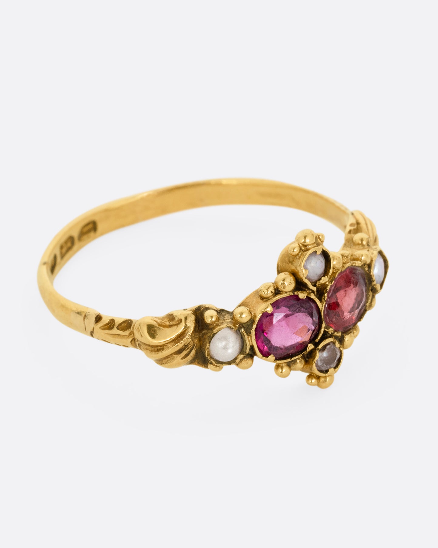 A yellow gold ring with garnets and seed pearls. Shown from the side.
