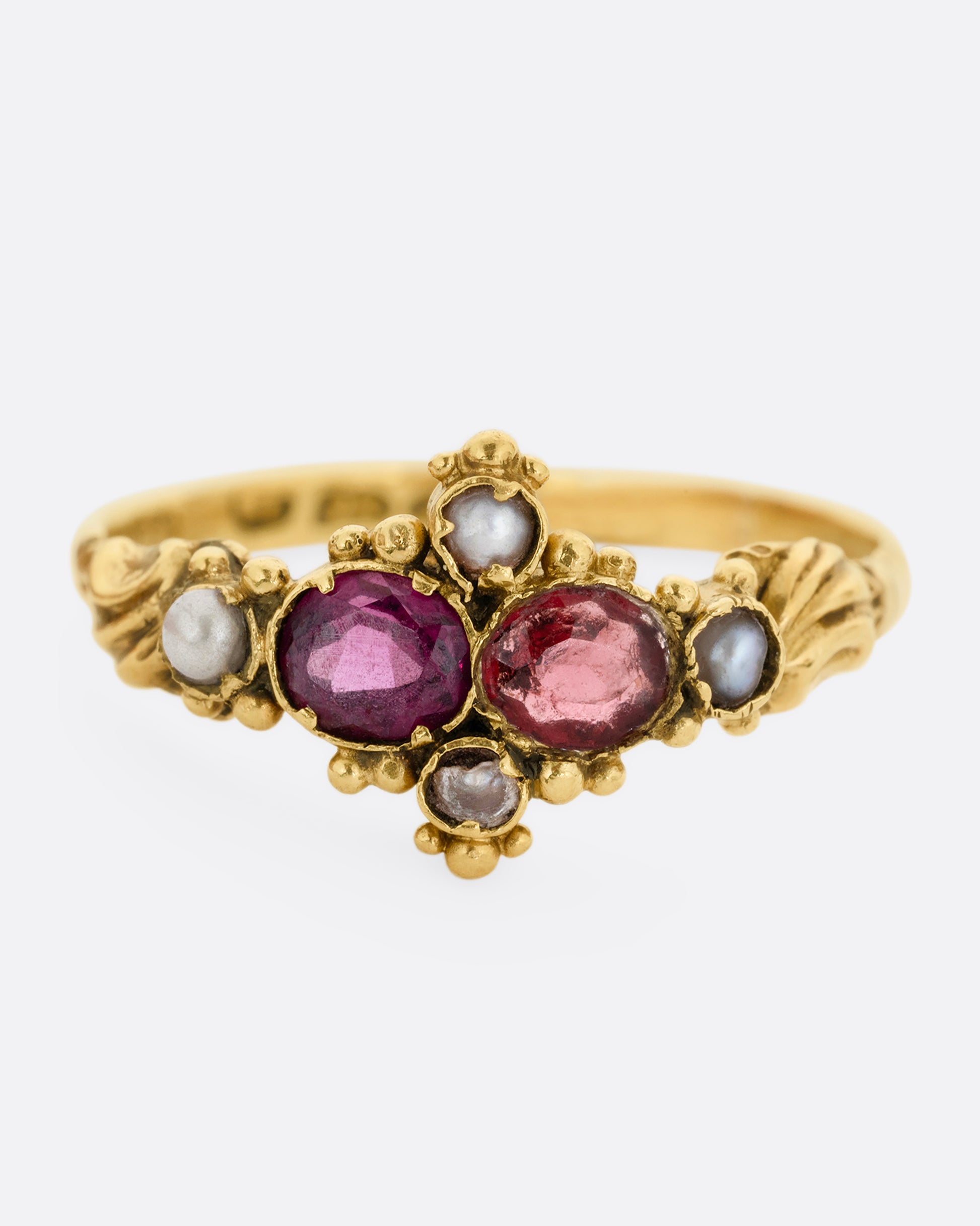 A yellow gold ring with garnets and seed pearls. Shown from the front.