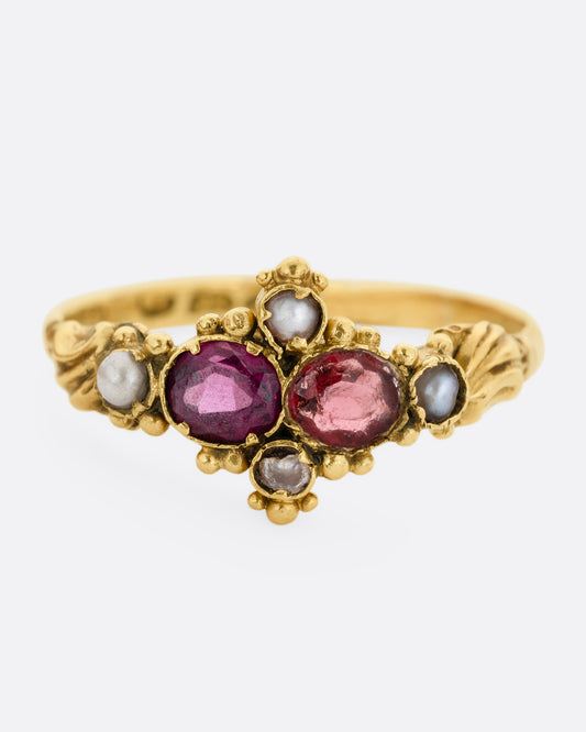 A yellow gold ring with garnets and seed pearls. Shown from the front.