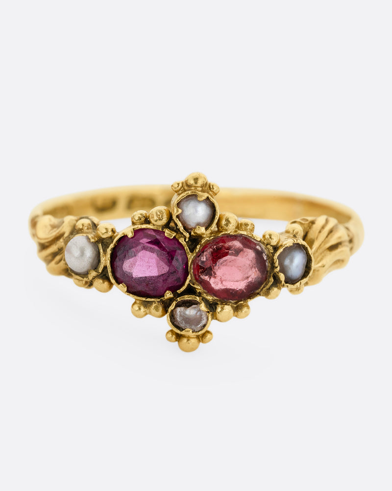 A yellow gold ring with garnets and seed pearls. Shown from the front.