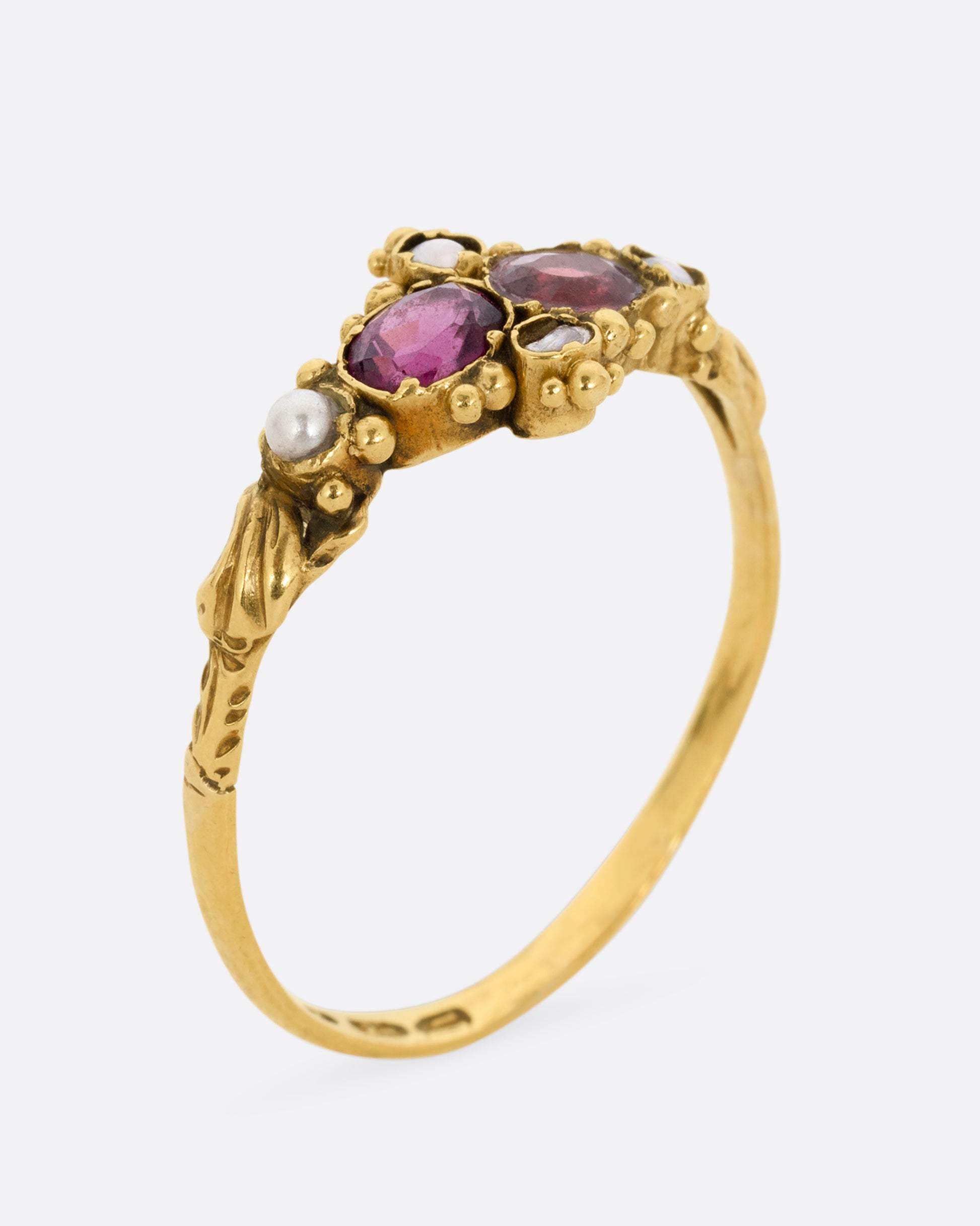 A yellow gold ring with garnets and seed pearls. Shown standing up from the side.