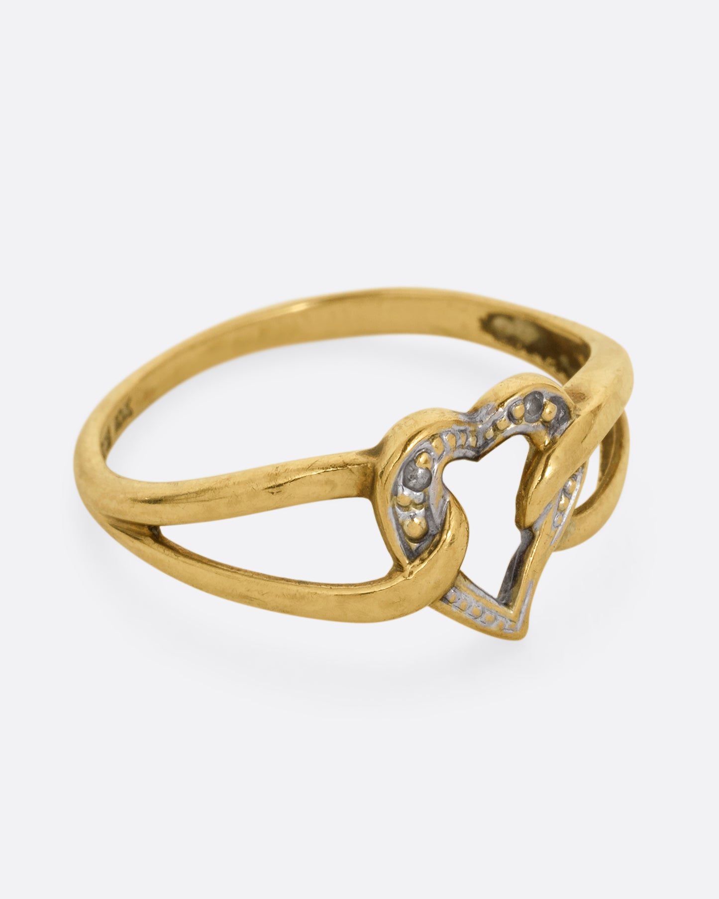 A yellow and white gold ring with an open heart and looped shoulders. Shown from the side.