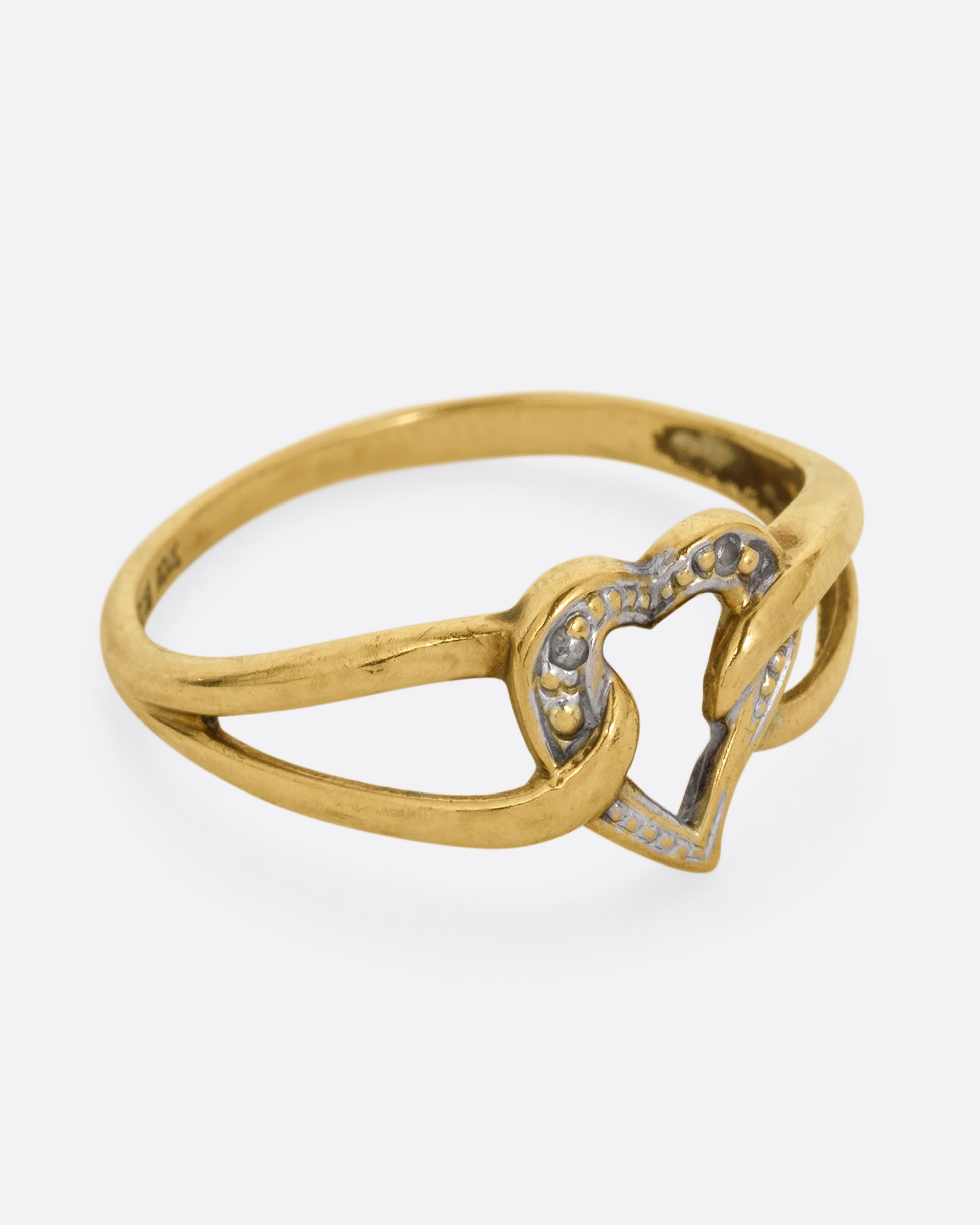A yellow and white gold ring with an open heart and looped shoulders. Shown from the side.