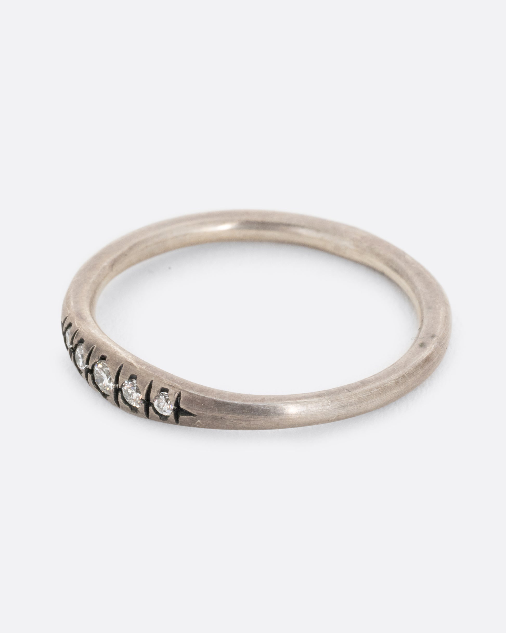 A silver ring with white diamonds and darkened engravings. Shown from the side.