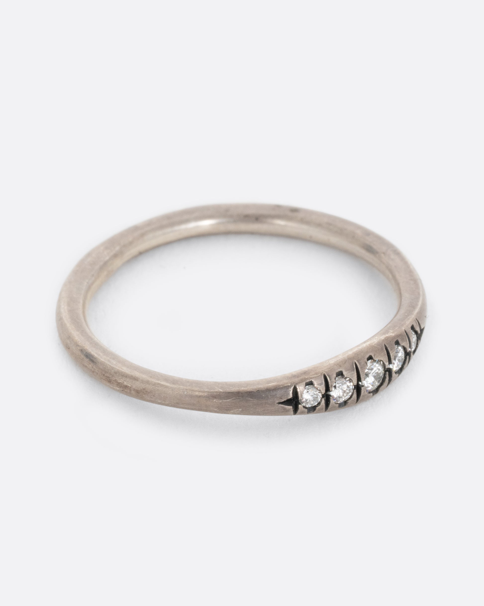 A silver ring with white diamonds and darkened engravings. Shown from the side.