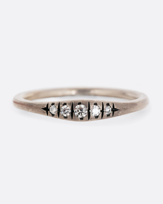 A silver ring with white diamonds and darkened engravings. Shown from the front.