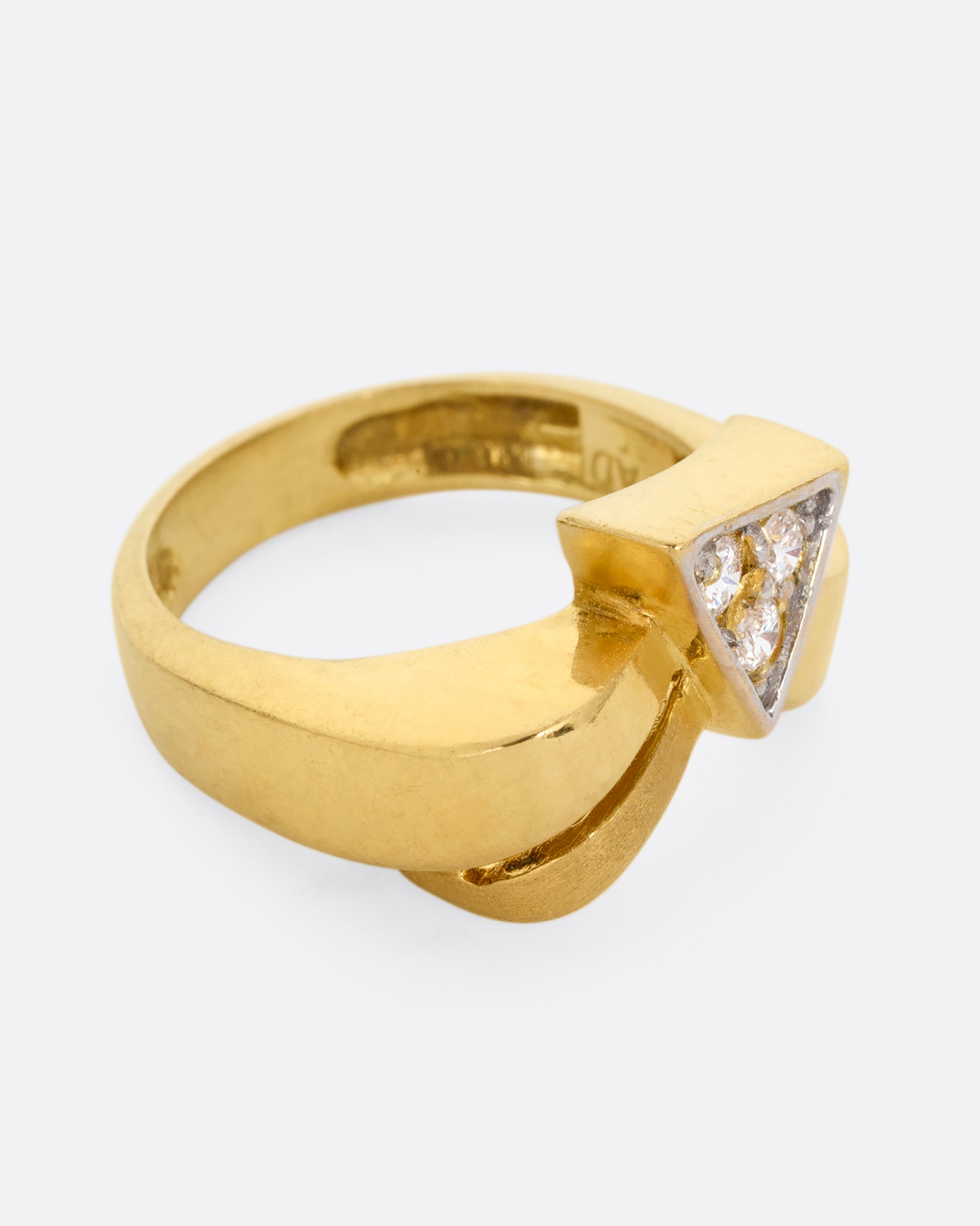A yellow gold ring with a curvy band and three diamonds set in a triangular shaped setting. Shown from the side.