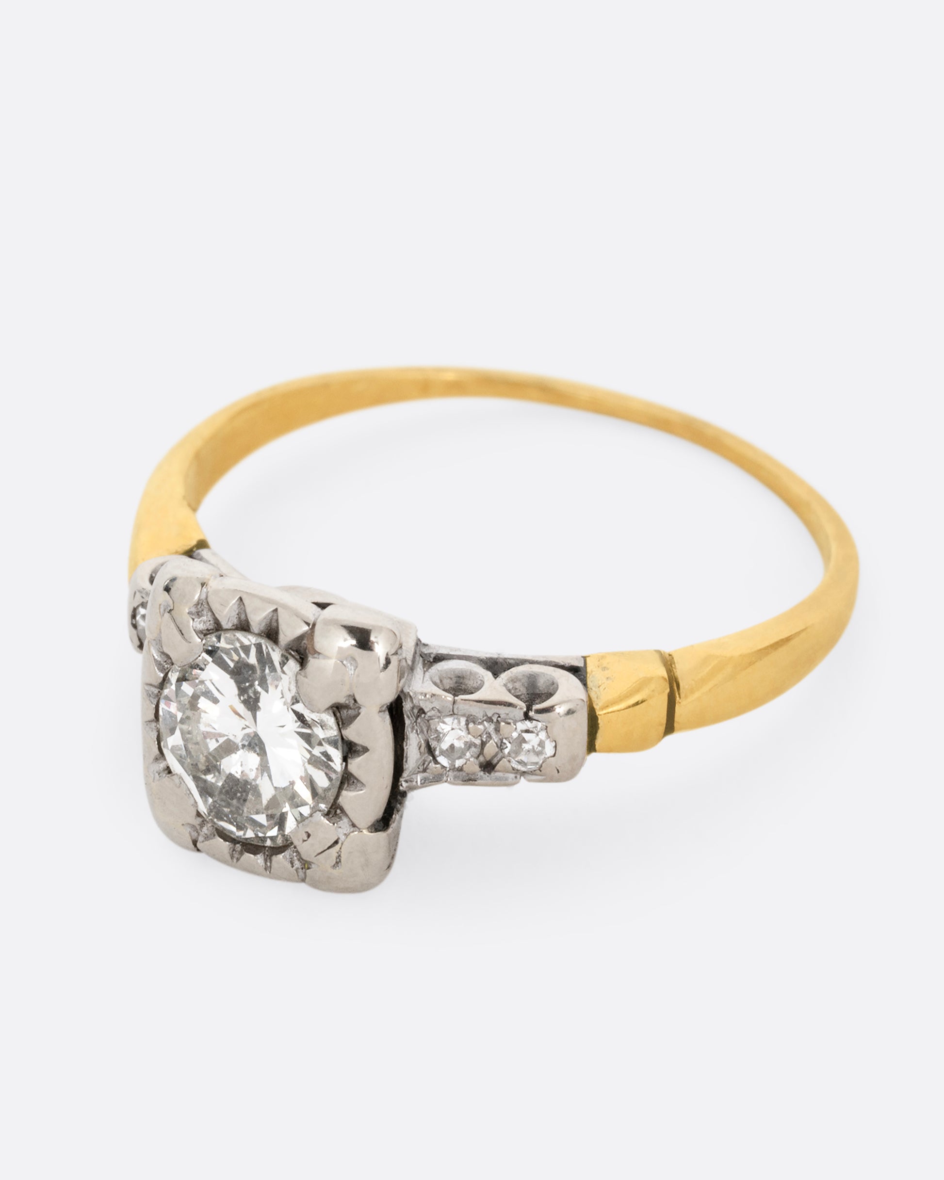 A yellow gold ring with a white gold setting and a round central diamond with four bead set diamonds on the shoulders. Shown from the side.