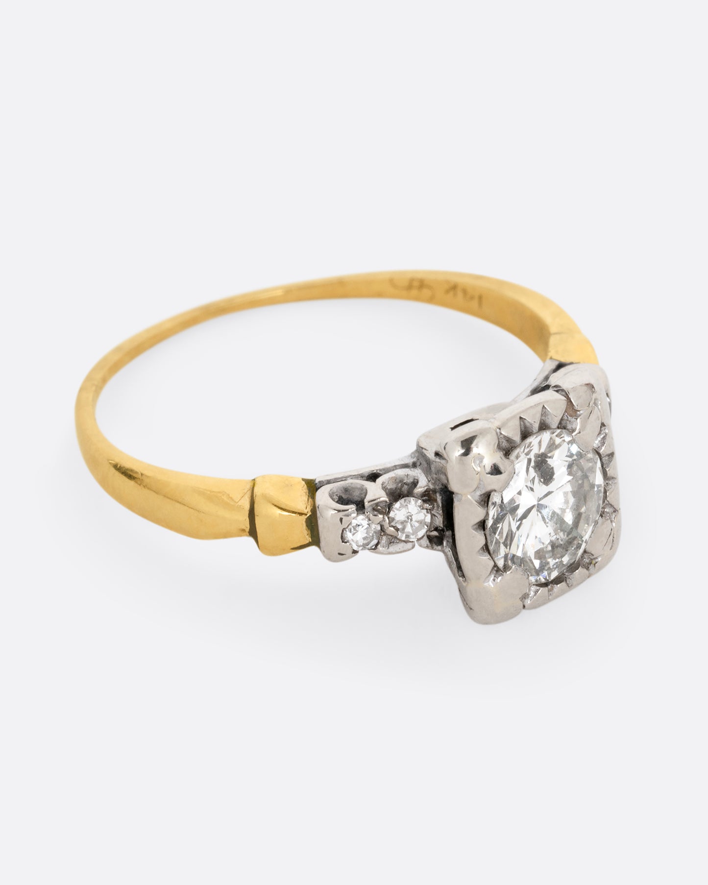 A yellow gold ring with a white gold setting and a round central diamond with four bead set diamonds on the shoulders. Shown from the side.
