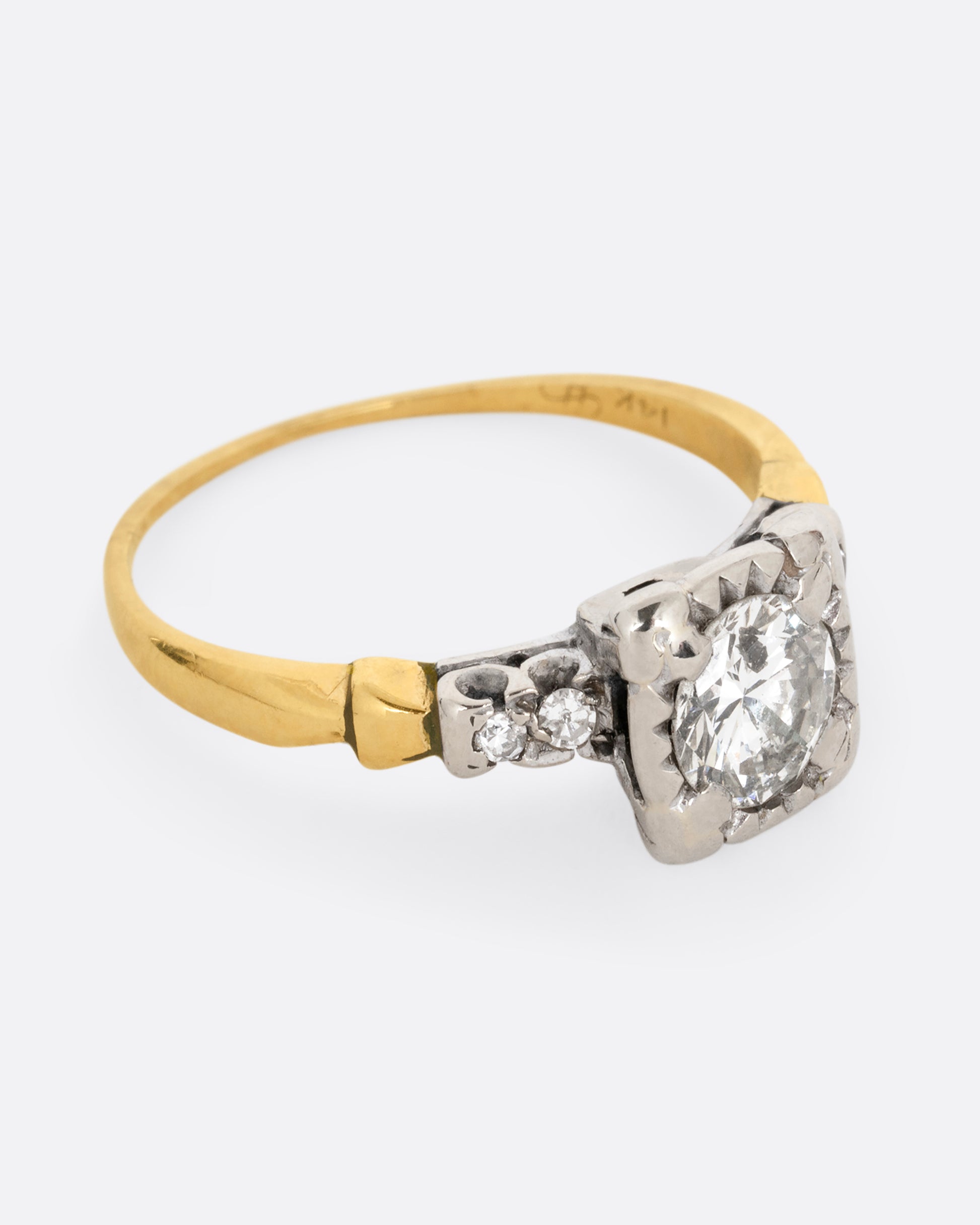 A yellow gold ring with a white gold setting and a round central diamond with four bead set diamonds on the shoulders. Shown from the side.