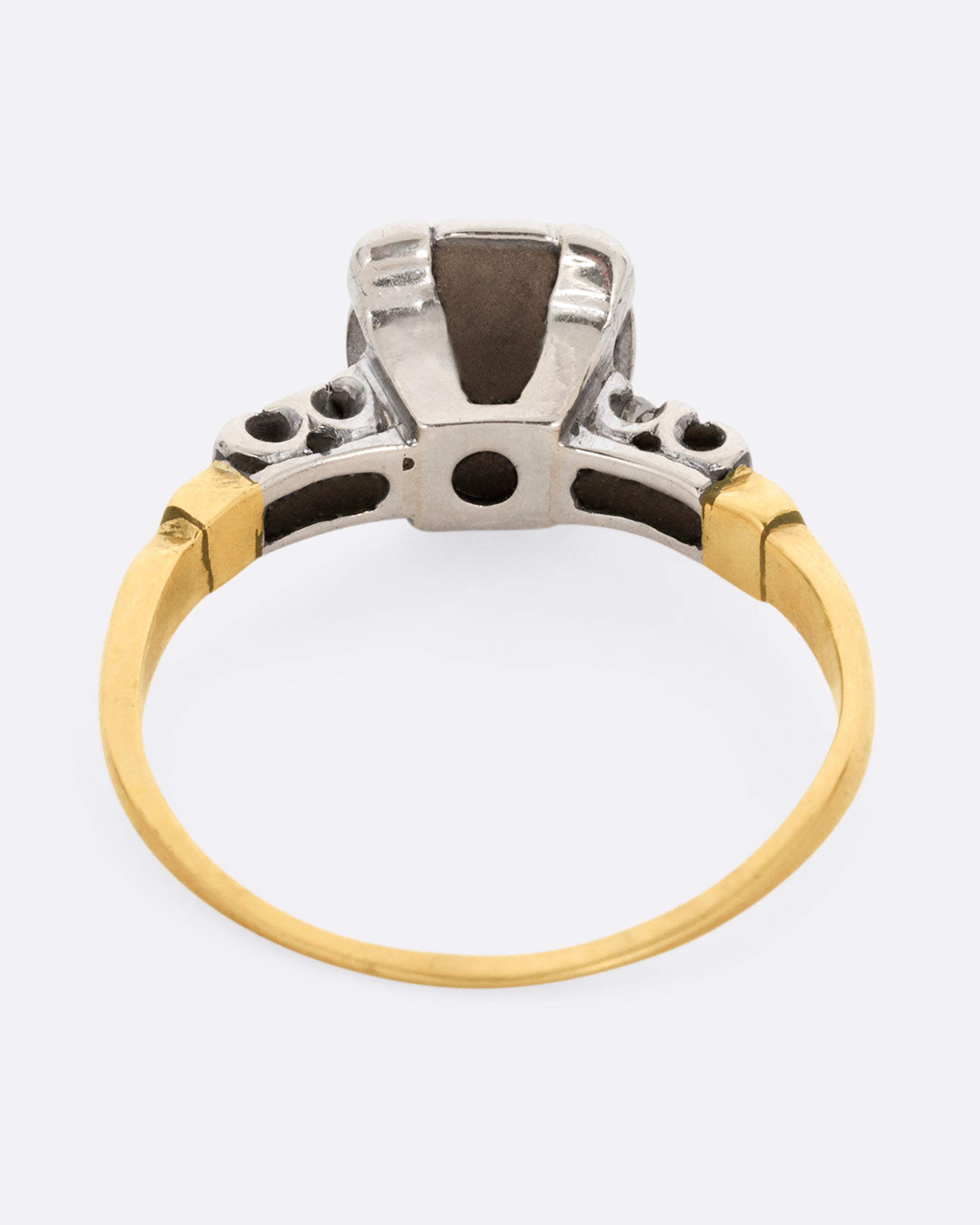 A yellow gold ring with a white gold setting and a round central diamond with four bead set diamonds on the shoulders. Shown from the back.