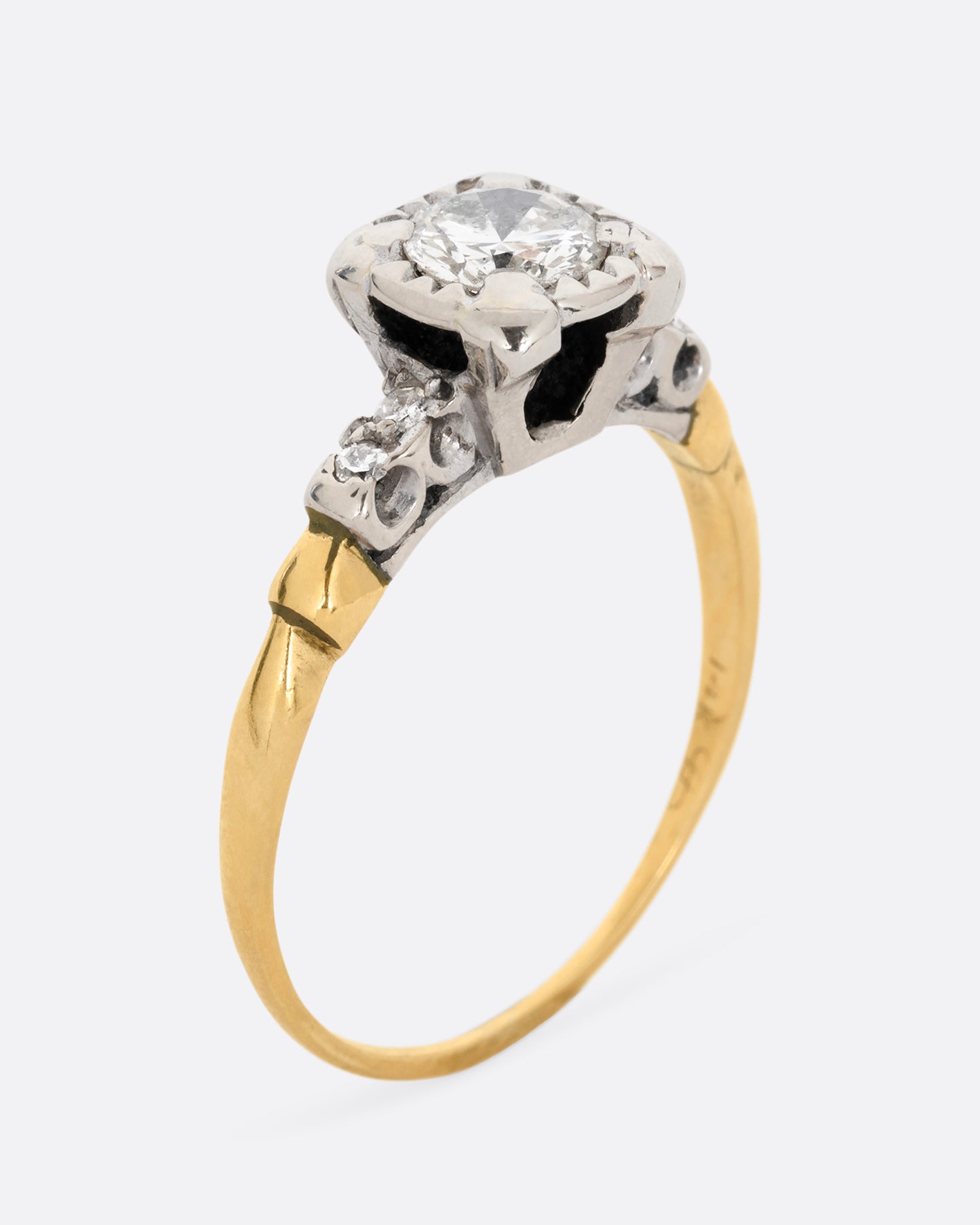 A yellow gold ring with a white gold setting and a round central diamond with four bead set diamonds on the shoulders. Shown standing up from the side.