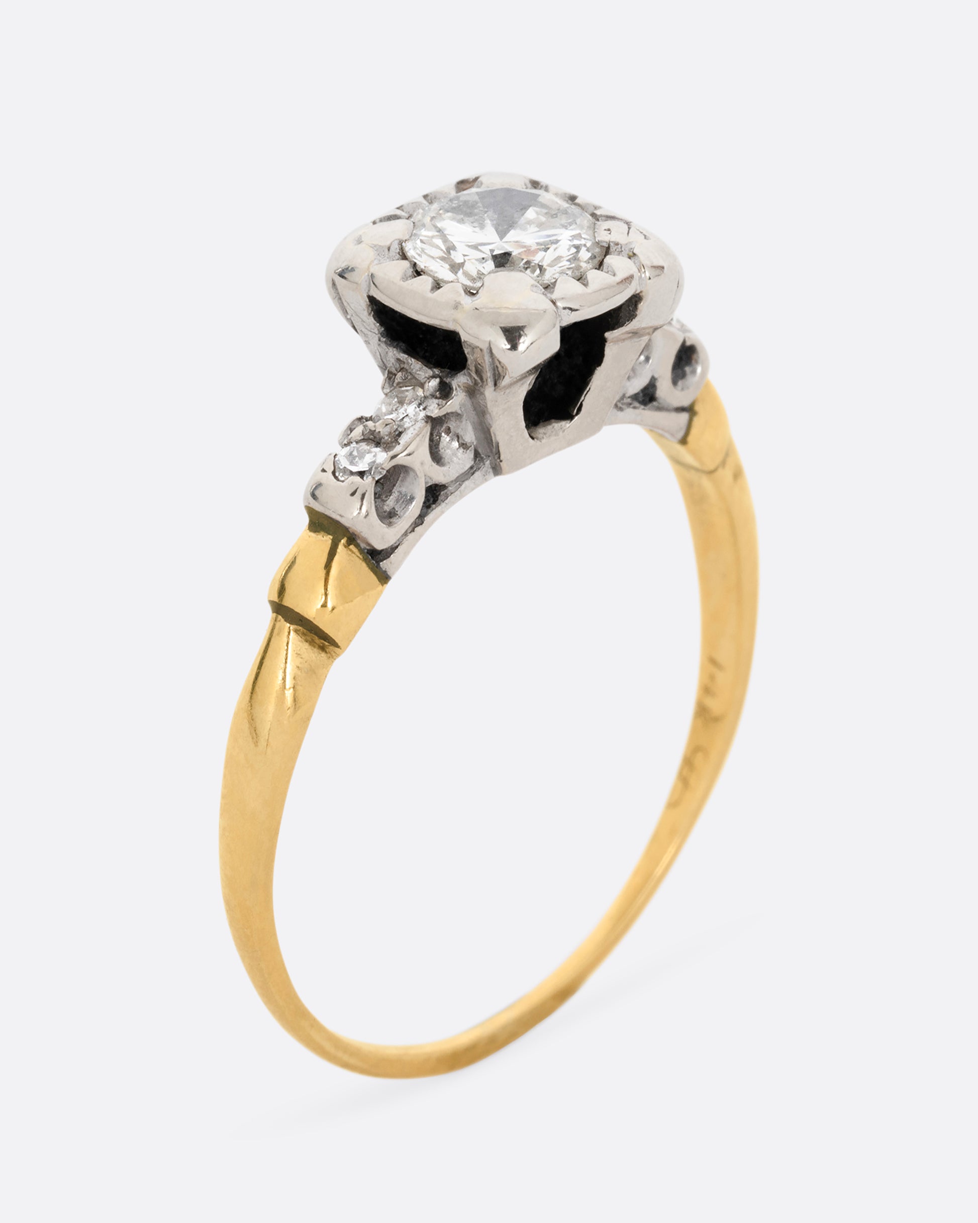 A yellow gold ring with a white gold setting and a round central diamond with four bead set diamonds on the shoulders. Shown standing up from the side.