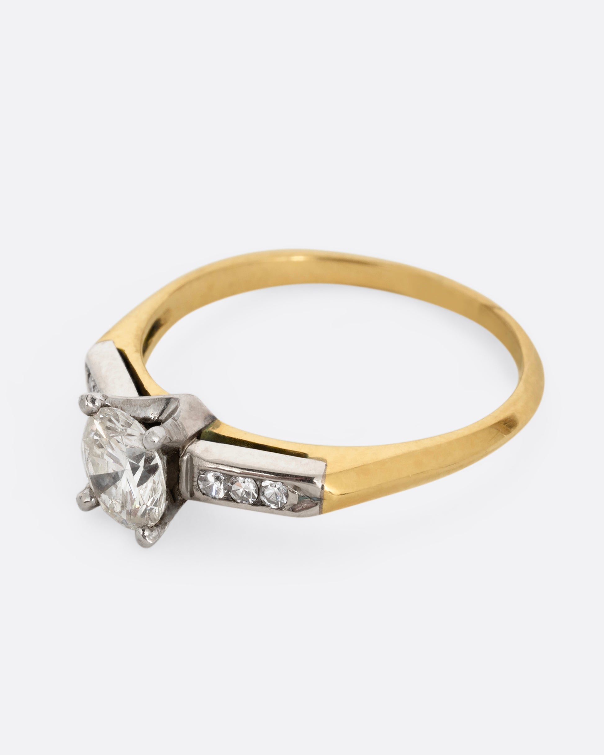 A yellow gold ring with white gold setting and six channel set diamonds with a central prong set brilliant cut diamond. Shown from the side.