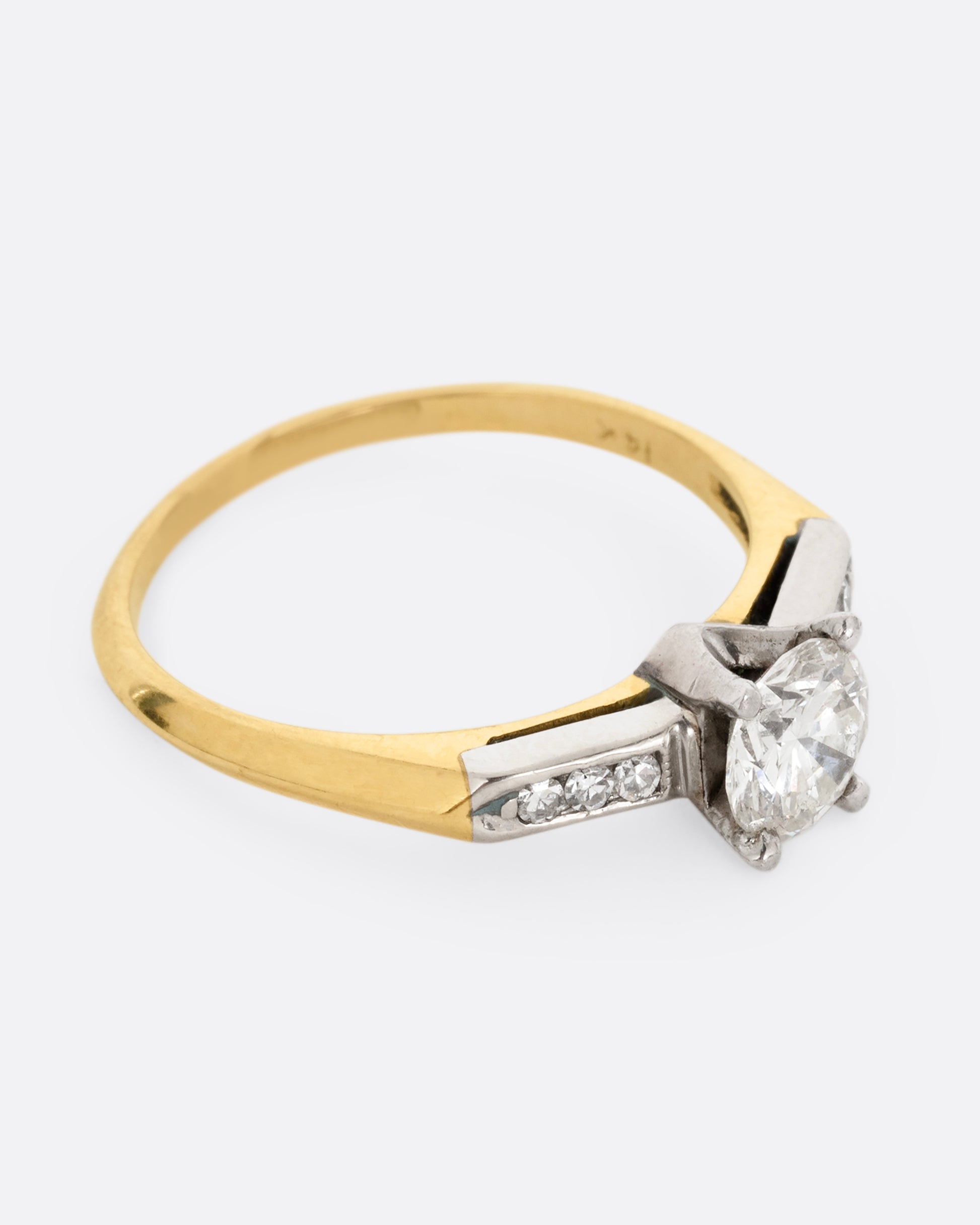 A yellow gold ring with white gold setting and six channel set diamonds with a central prong set brilliant cut diamond. Shown from the side.