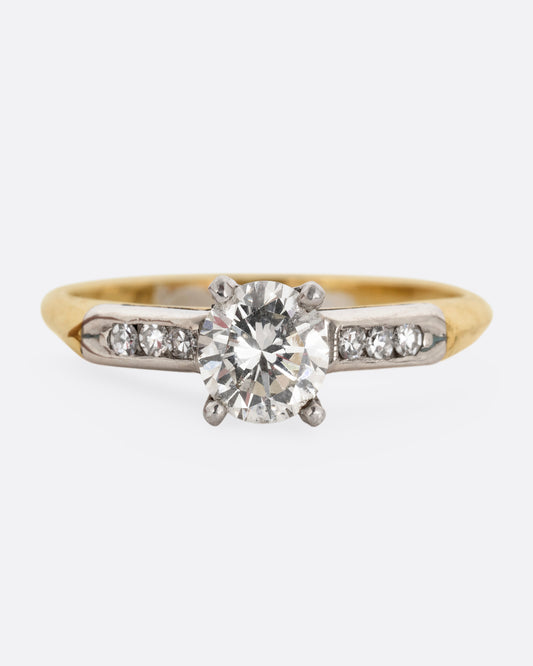 A yellow gold ring with white gold setting and six channel set diamonds with a central prong set brilliant cut diamond. Shown from the front.