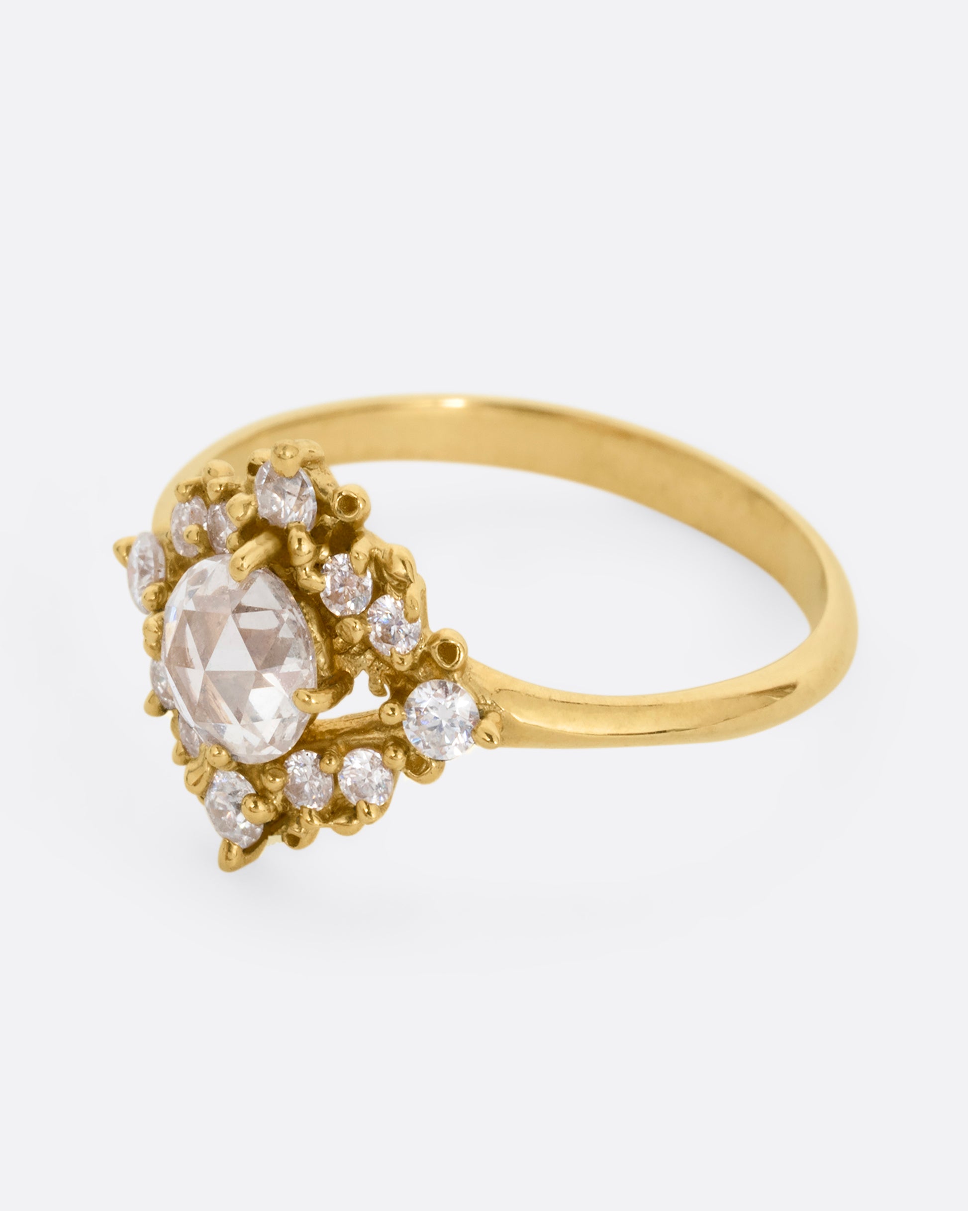 A yellow gold ring with a rose cut center diamond surrounded by round diamonds. Shown from the side.
