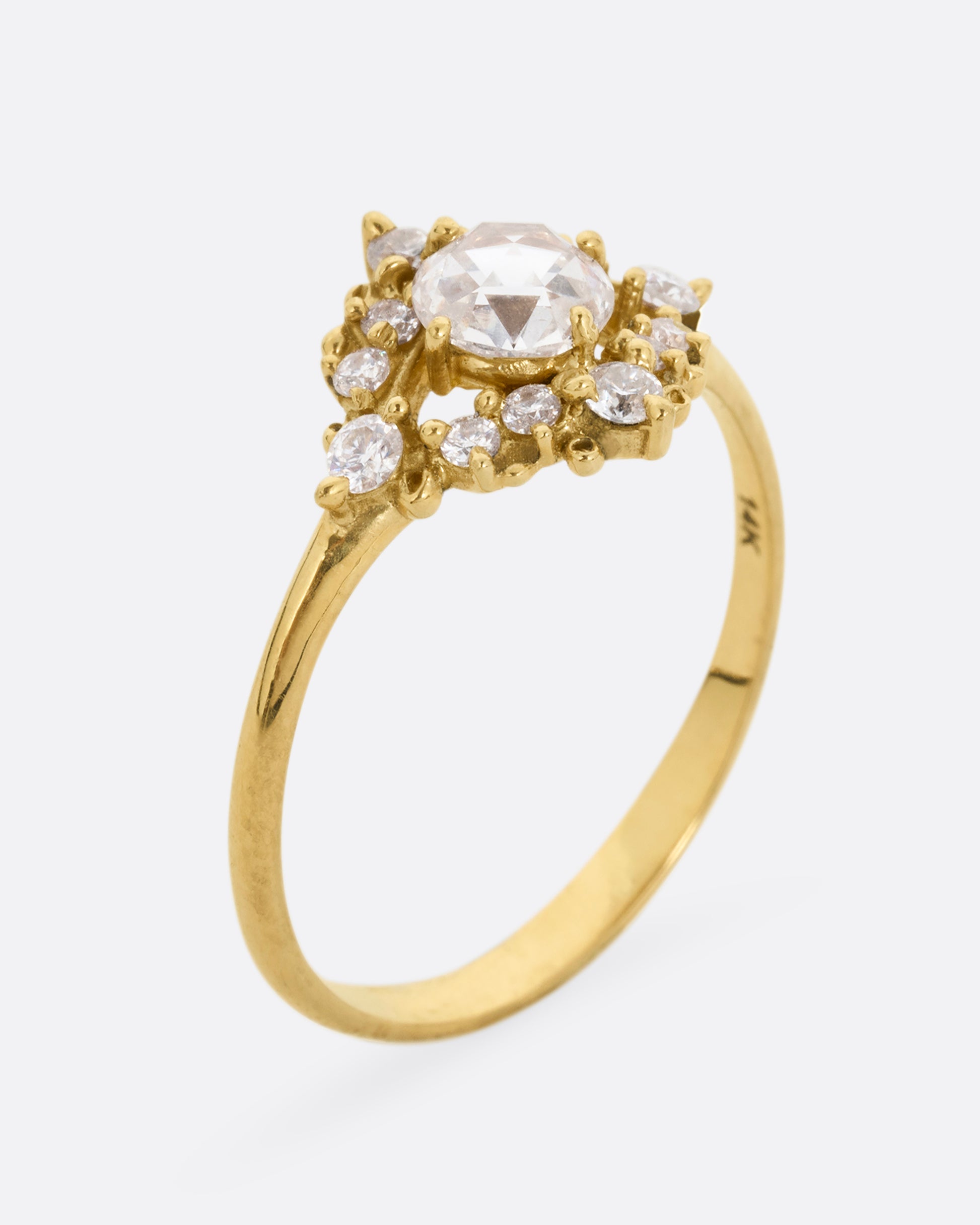 A yellow gold ring with a rose cut center diamond surrounded by round diamonds. Shown standing up from the side.