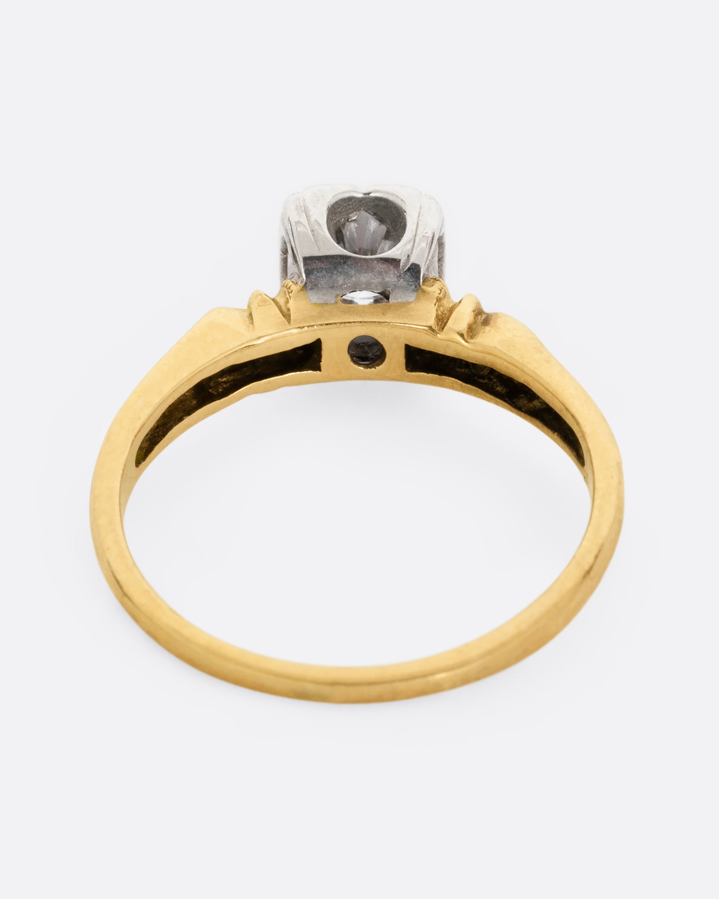 A yellow gold ring with intricately detailed shoulders and a white gold set center diamond. Shown from the back.