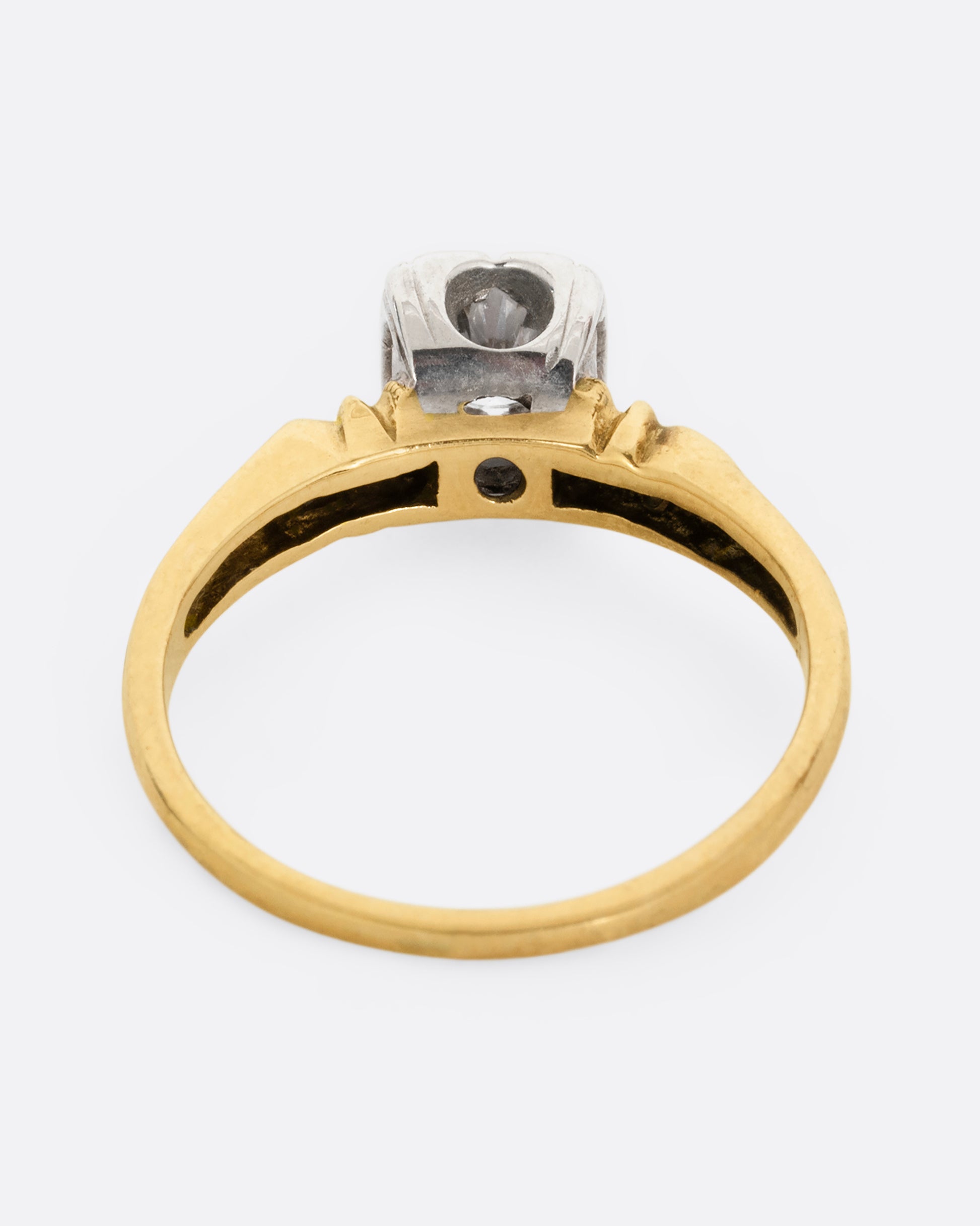 A yellow gold ring with intricately detailed shoulders and a white gold set center diamond. Shown from the back.
