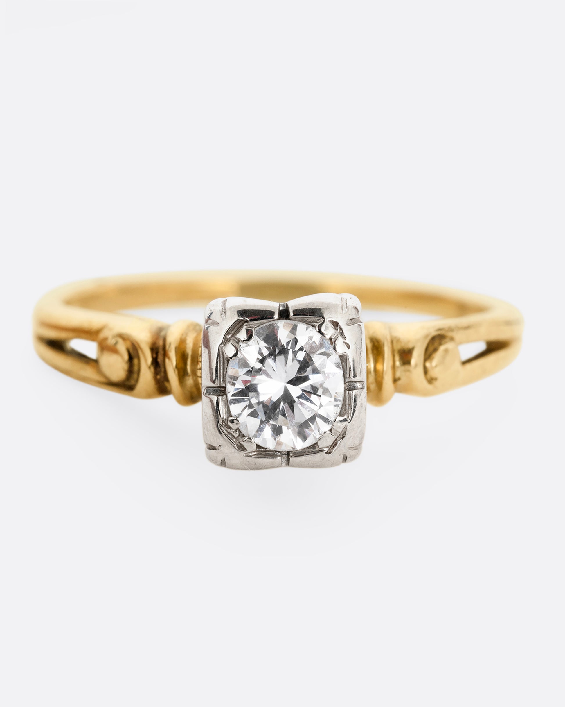 A yellow gold ring with intricately detailed shoulders and a white gold set center diamond. Shown from the front.