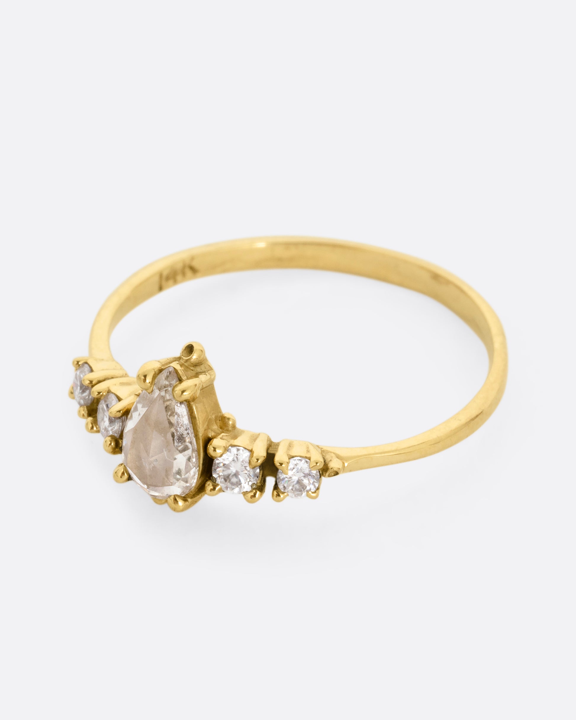  A yellow gold ring with a pear shaped champagne diamond with round white diamond accents. Shown from the side.