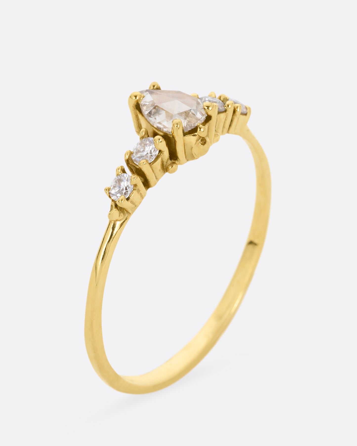  A yellow gold ring with a pear shaped champagne diamond with round white diamond accents. Shown standing up from the side.