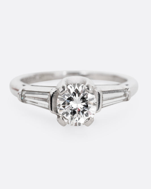 A platinum ring with a brilliant cut prong set diamond and two baguette diamonds. Shown from the front.