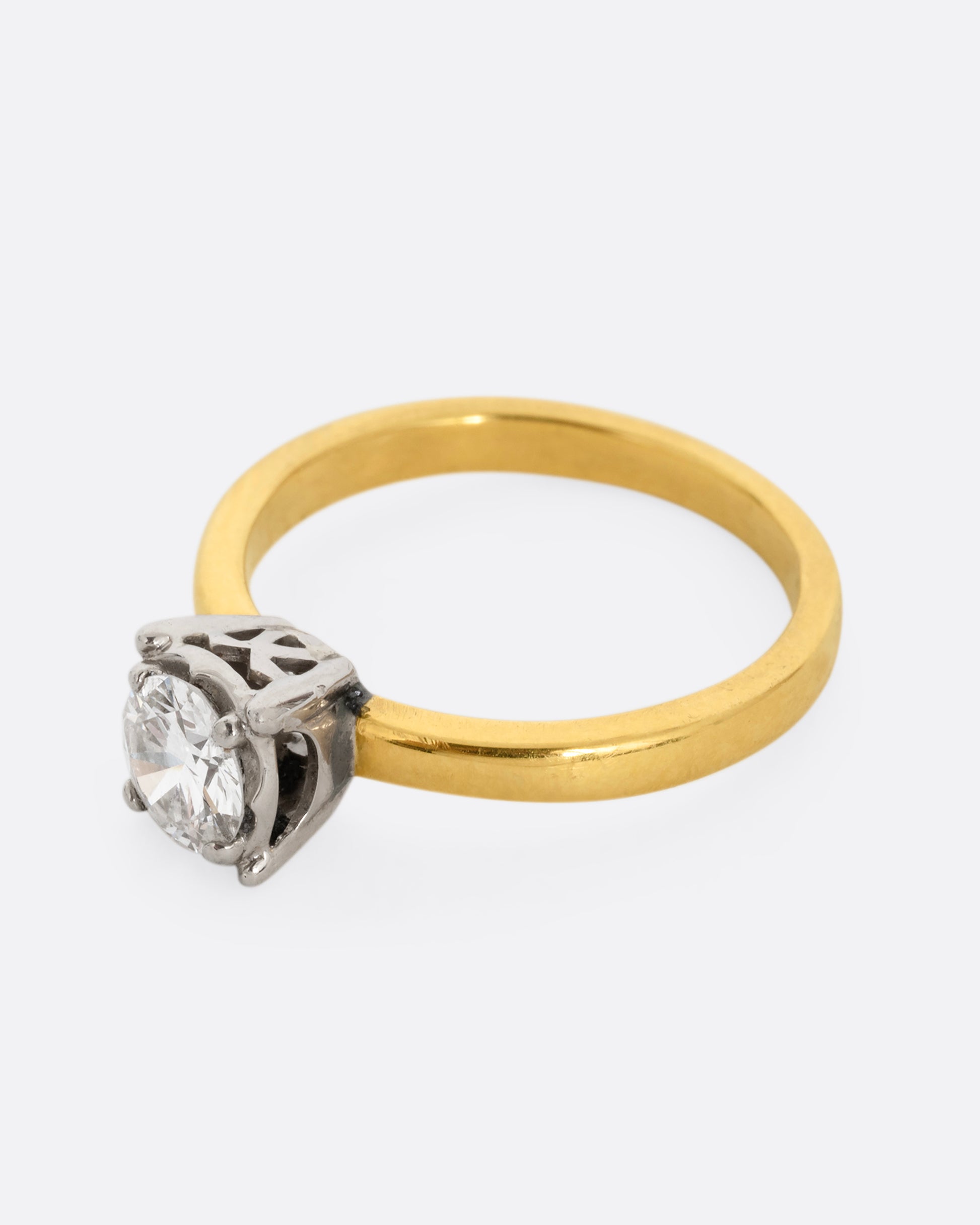 A yellow gold ring with a white gold prong setting and a brilliant cut diamond. Shown from the side.