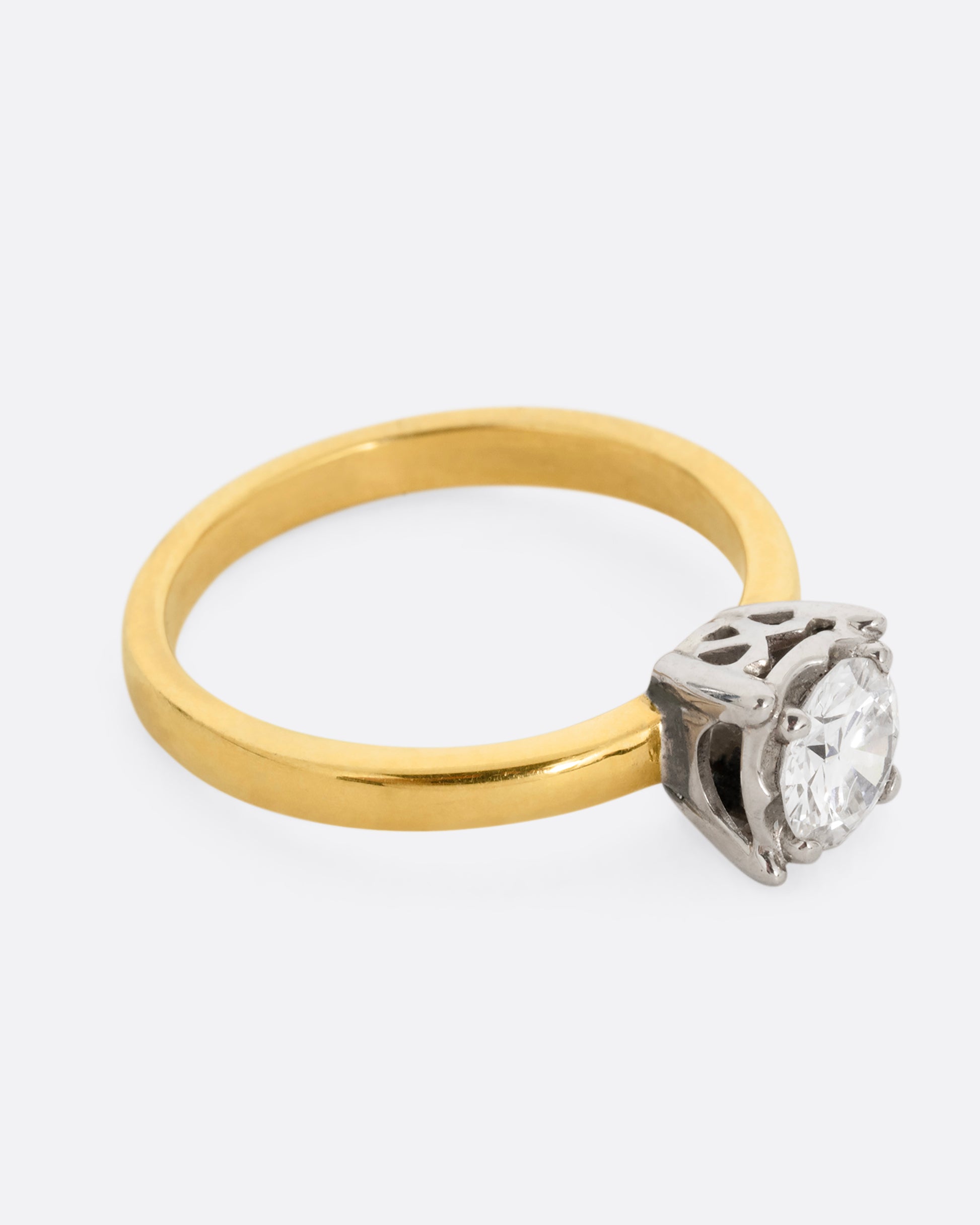 A yellow gold ring with a white gold prong setting and a brilliant cut diamond. Shown from the side.