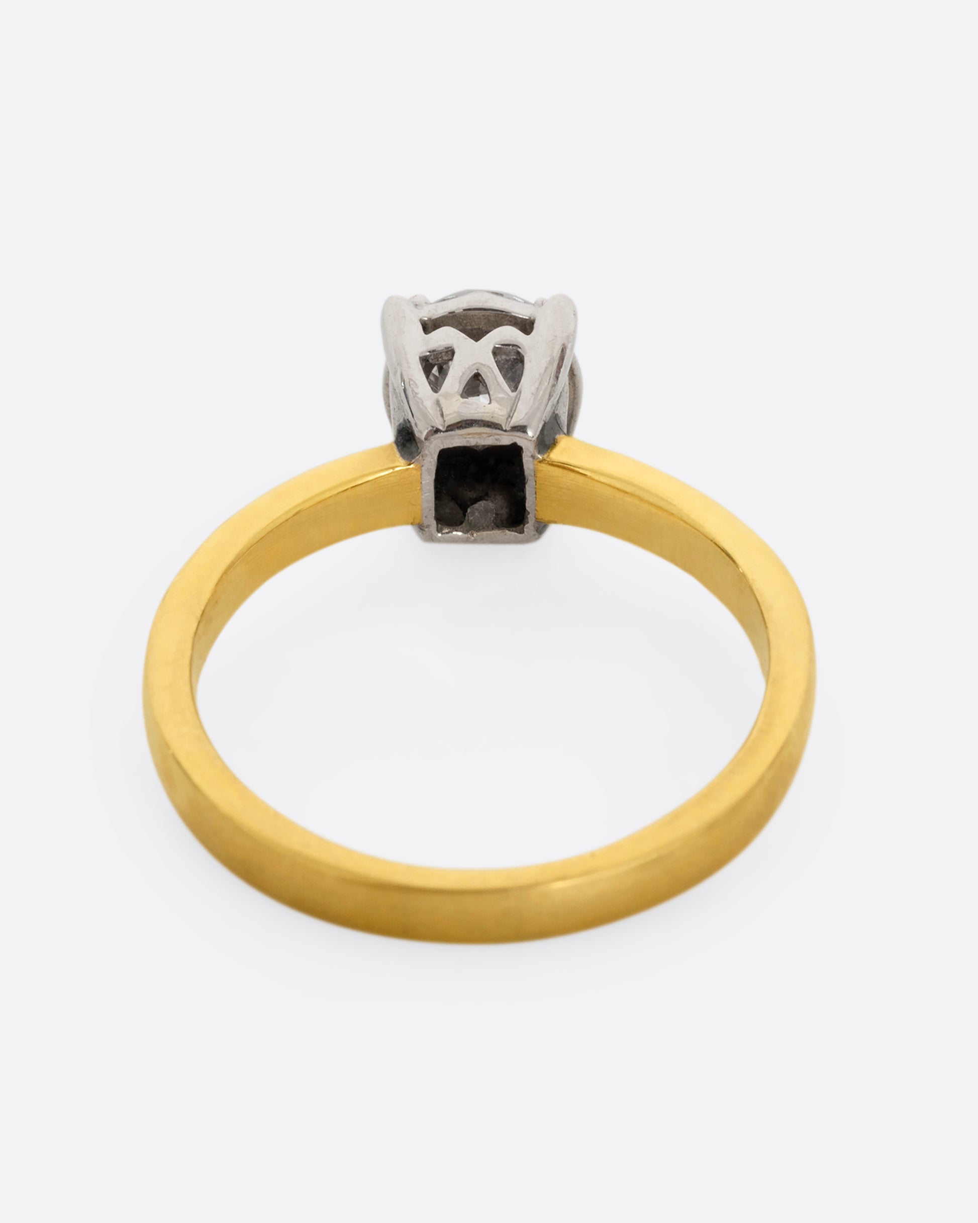 A yellow gold ring with a white gold prong setting and a brilliant cut diamond. Shown from the back.