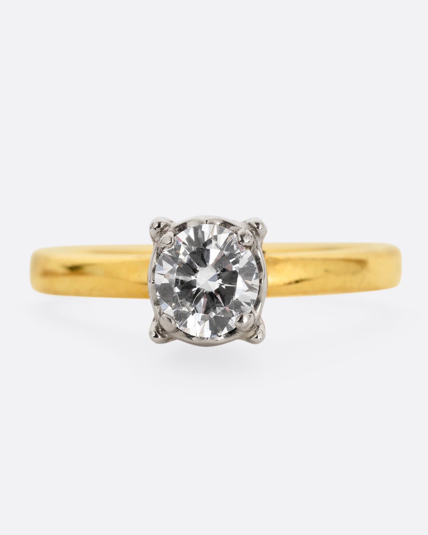 A yellow gold ring with a white gold prong setting and a brilliant cut diamond. Shown from the front.