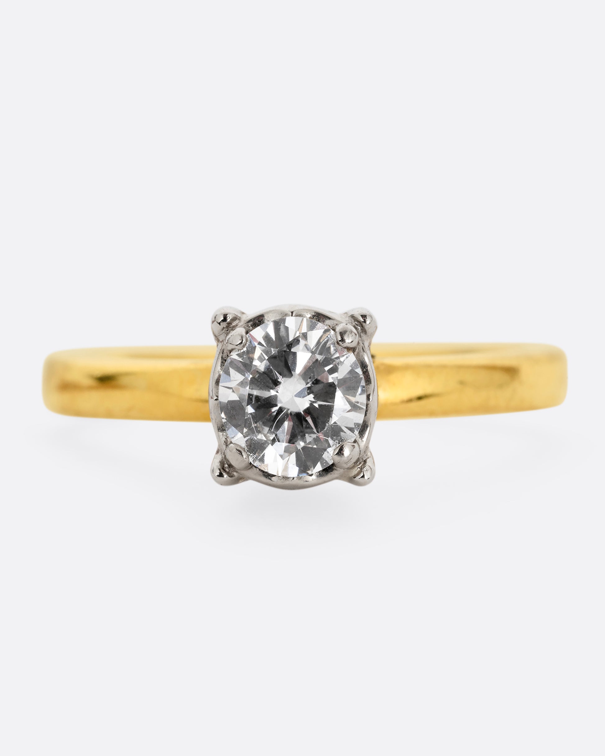 A yellow gold ring with a white gold prong setting and a brilliant cut diamond. Shown from the front.