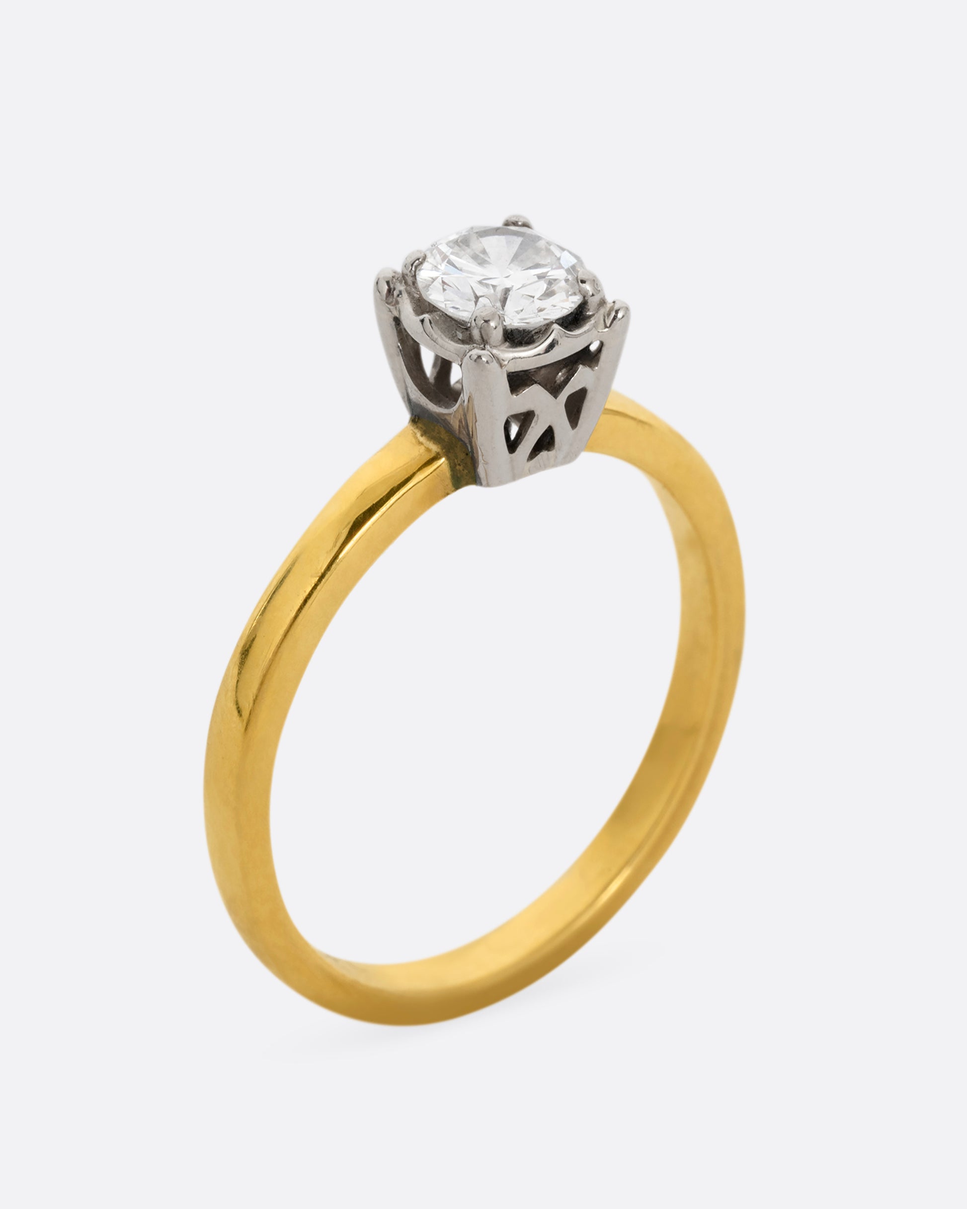 A yellow gold ring with a white gold prong setting and a brilliant cut diamond. Shown standing up from the side.