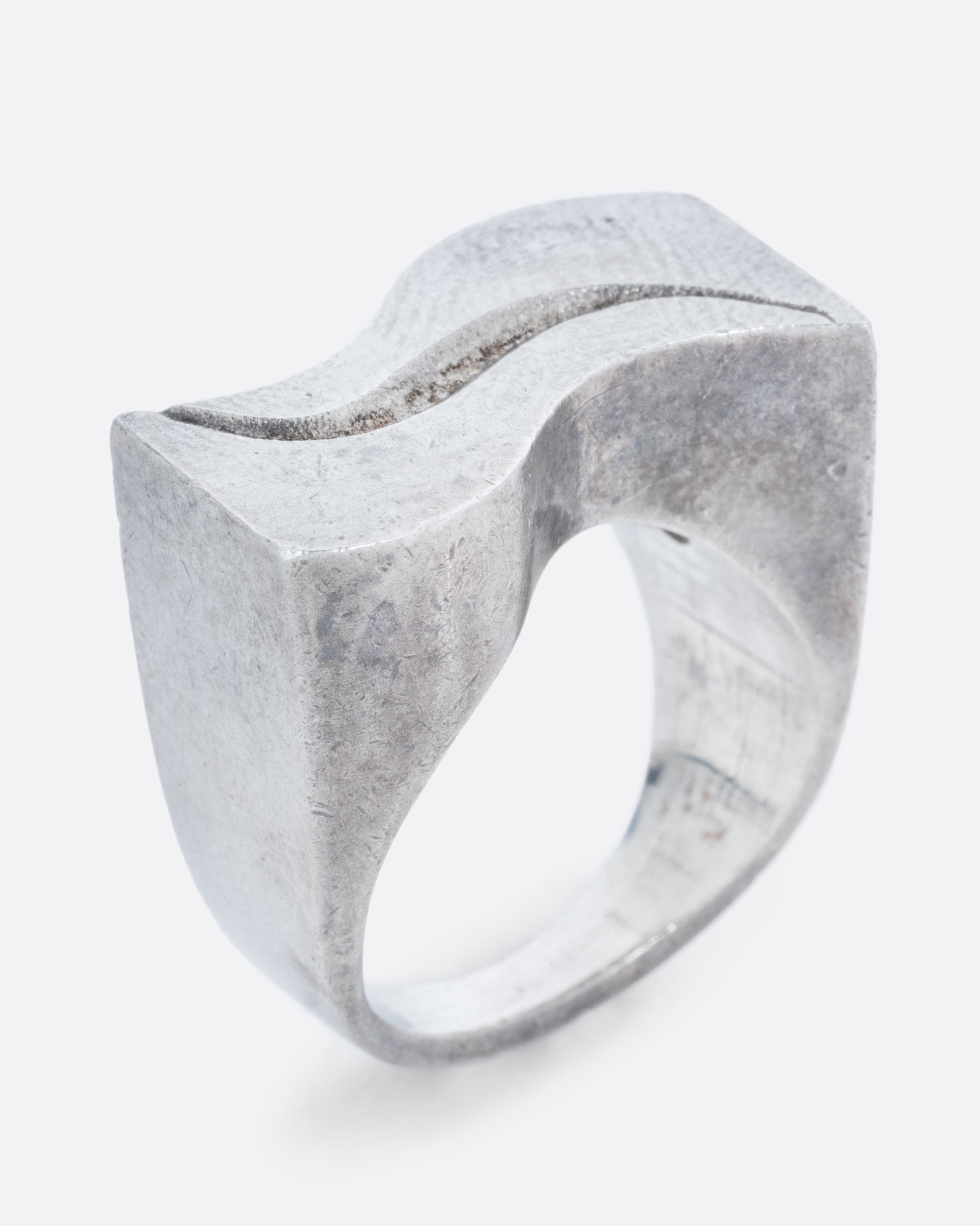 A silver ring with two waves on its face. Shown standing up from the side.
