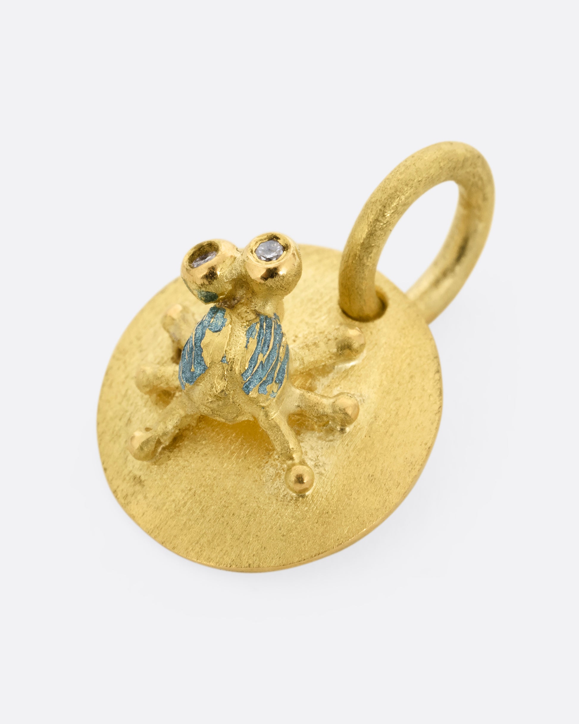 A yellow gold medallion with a diamond eyed bug with blue enamel striped wings. Shown lying flat.