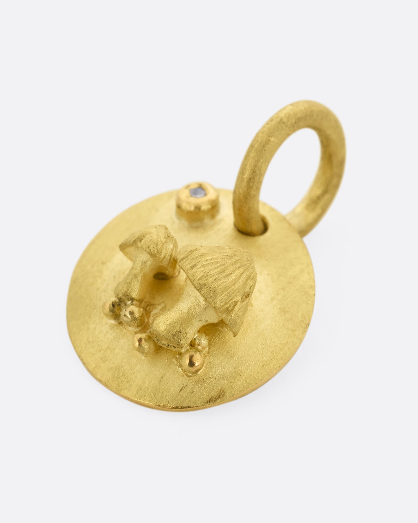 A yellow gold medallion with a diamond and mushrooms. Shown lying flat.