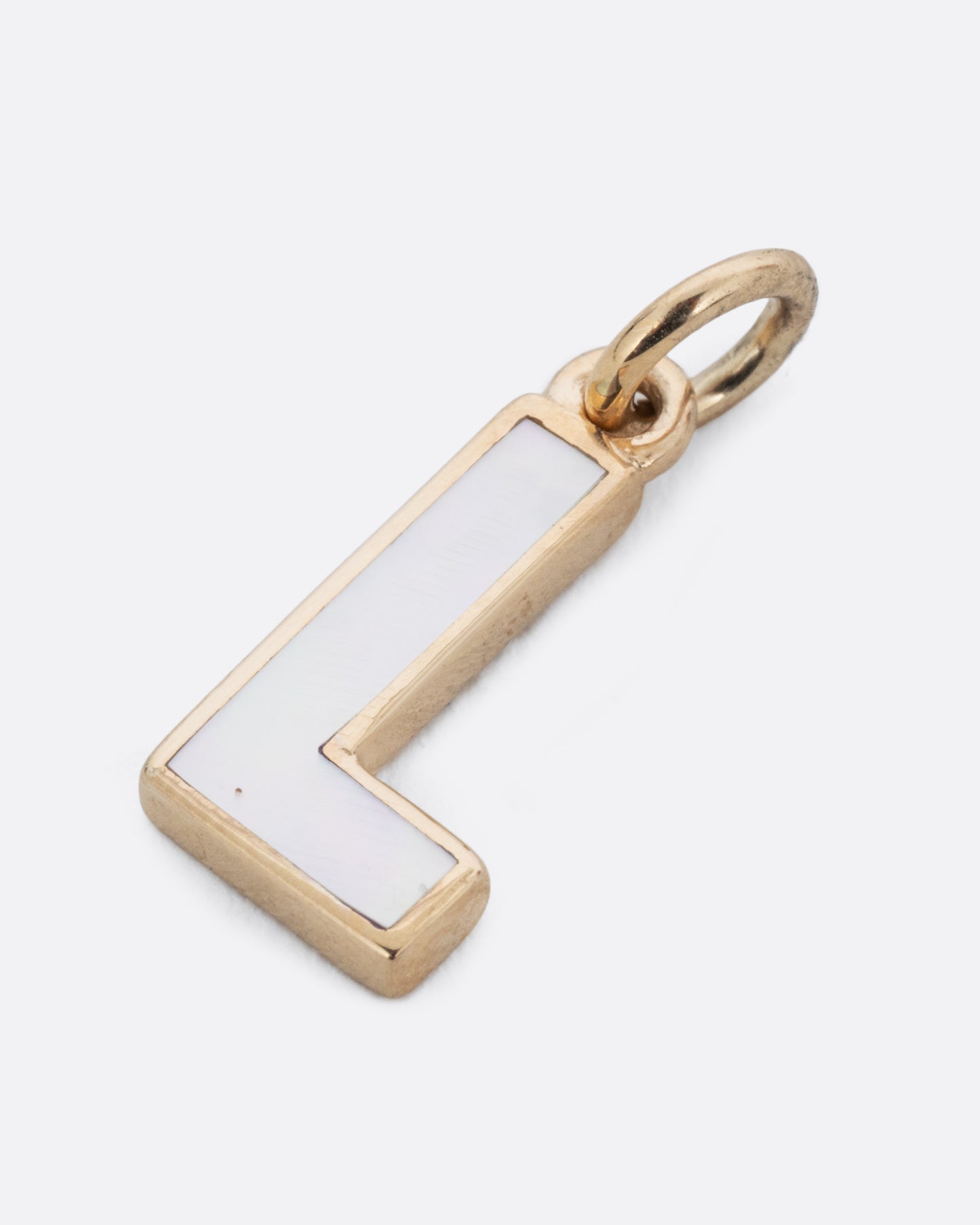 A mother of pearl inlaid L charm set in yellow gold with a yellow gold jump ring and bail. Shown lying flat from the front.