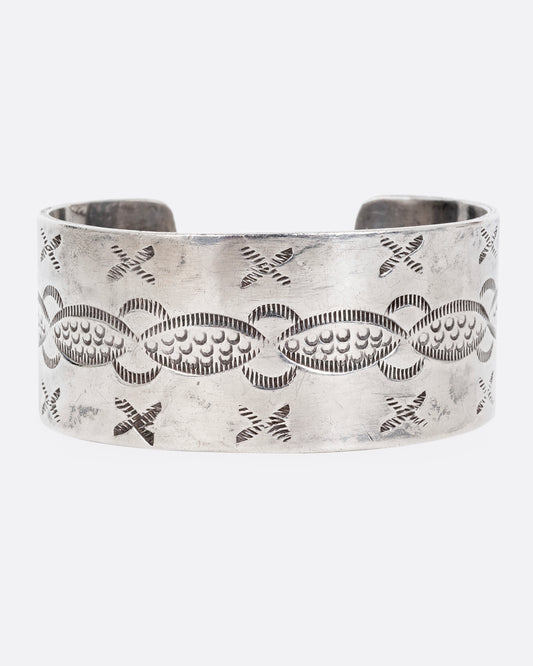 A wide silver cuff bracelet with stamping. Shown on its side from the front.