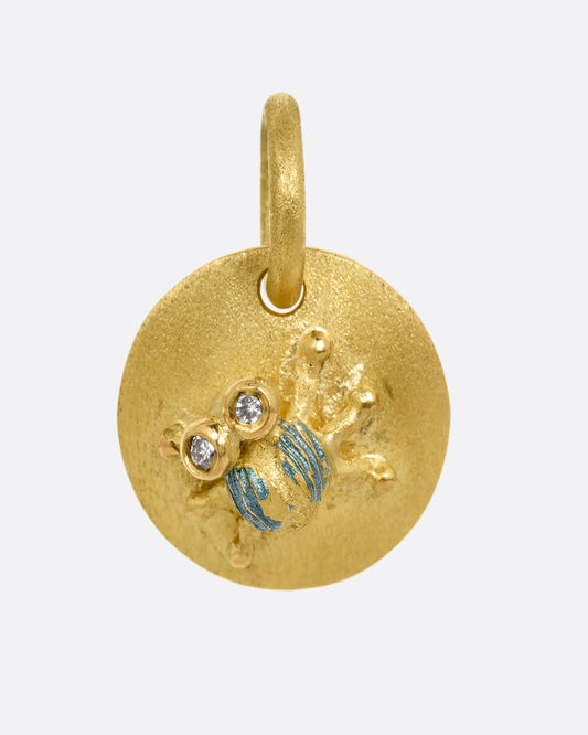 A yellow gold medallion with a diamond eyed bug with blue enamel striped wings. Shown from the front.