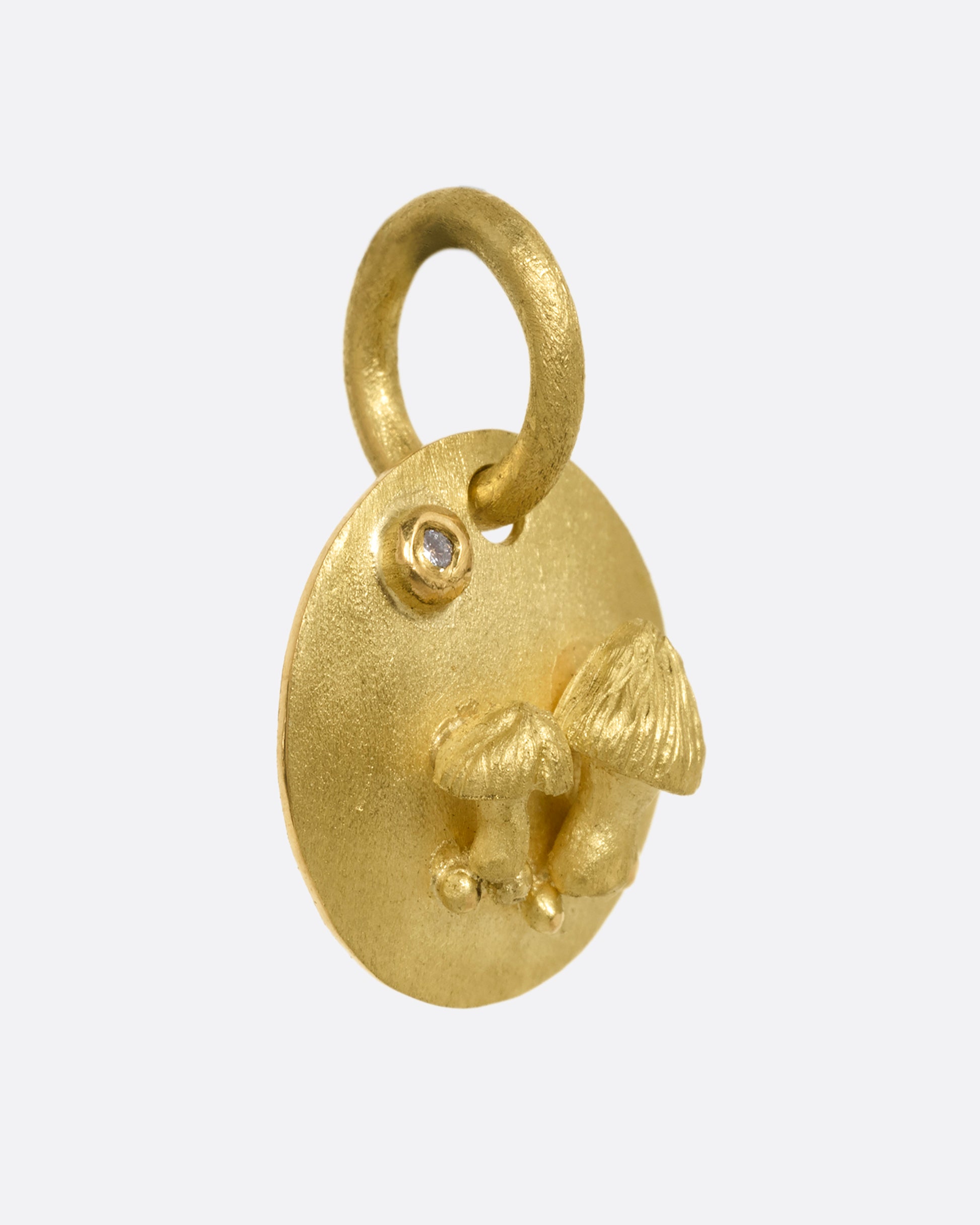 A yellow gold medallion with a diamond and mushrooms. Shown from the side.
