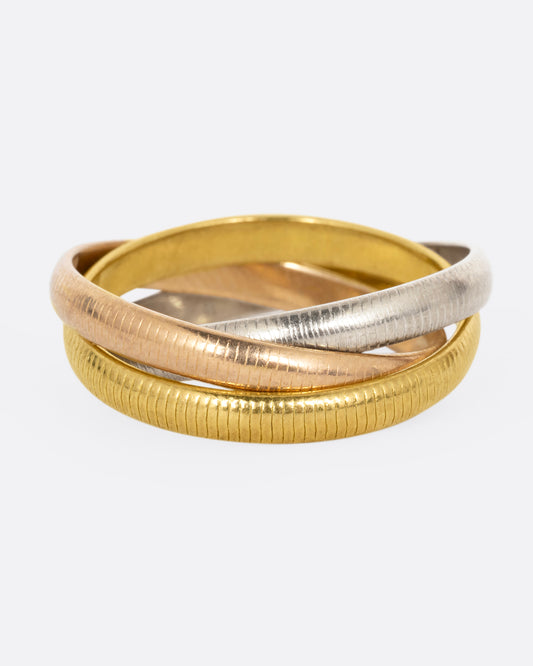 A Cartier Trinity Ring with three interlocking ribbed, textural bands in yellow, rose, and white gold. Each band rolls freely over its companions. Shown from the front.