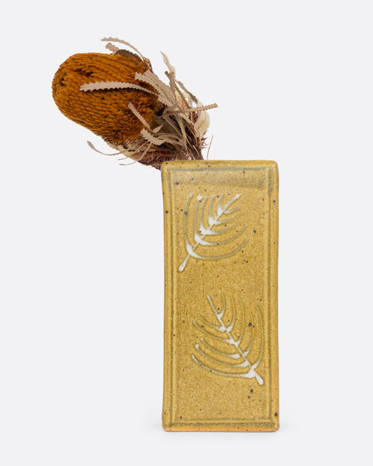 A yellow rectangular vase with botanical imagery. Shown with a flower in it from the front.