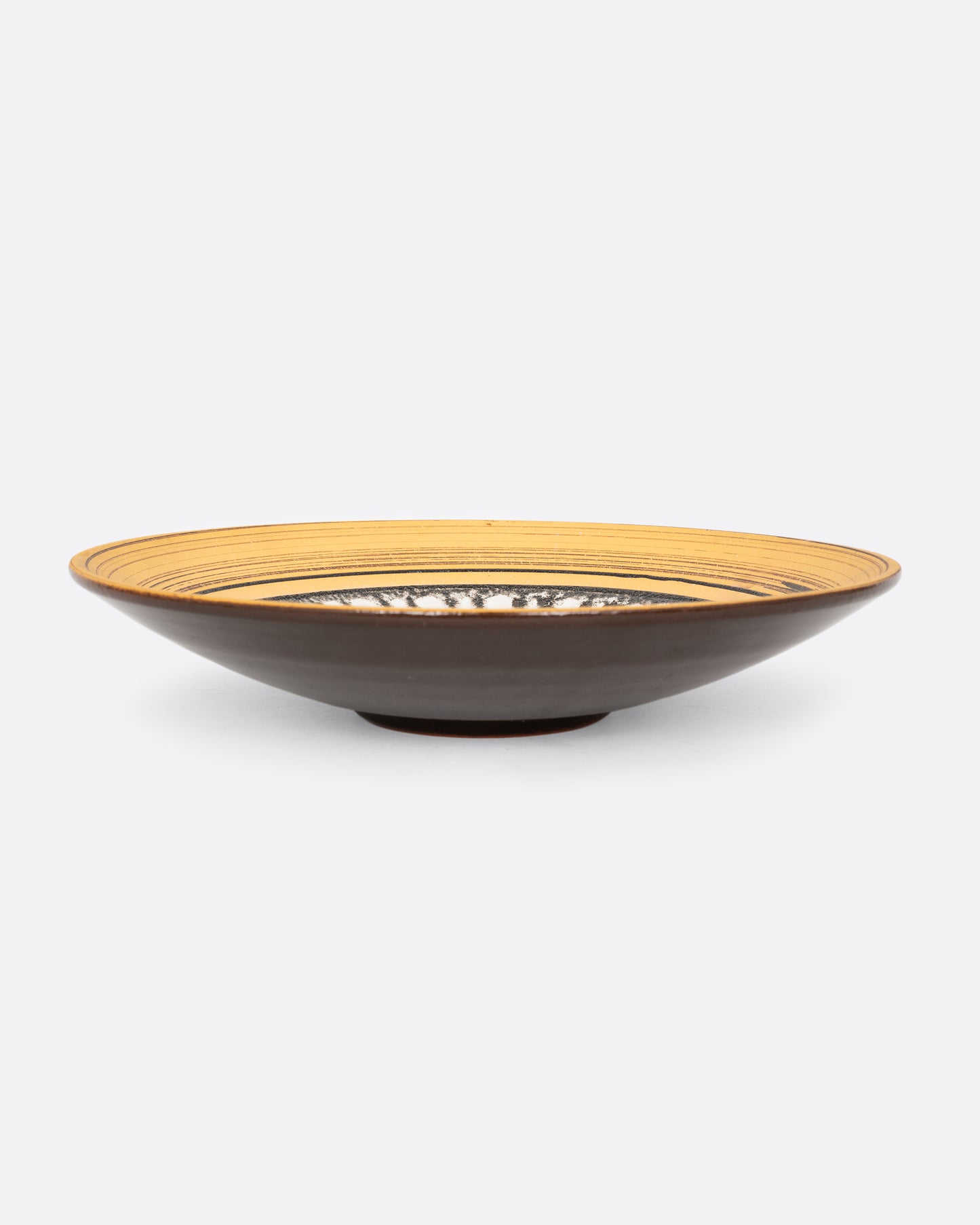 A round serving plate with a sun motif in yellow, brown, and white. Shown from the side.