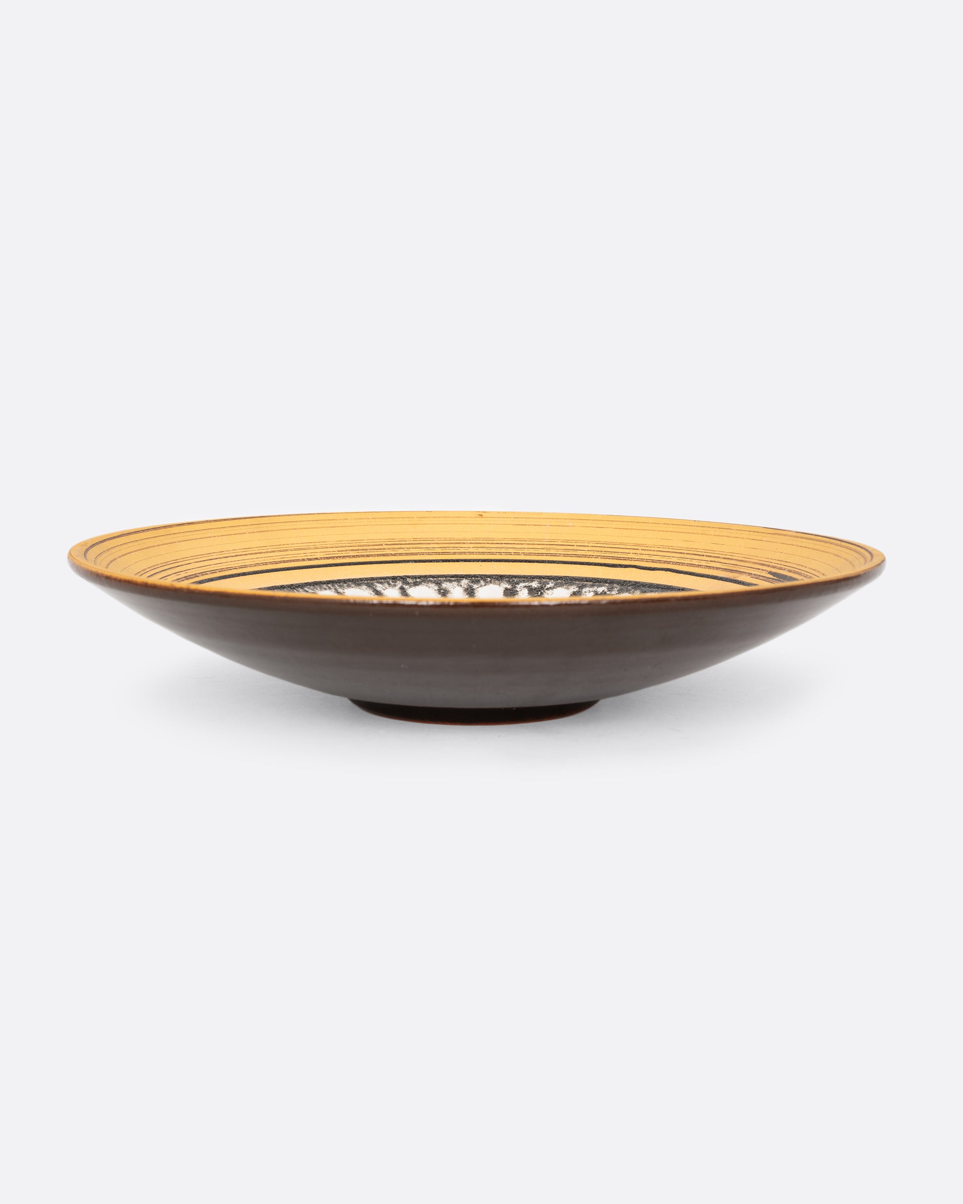 A round serving plate with a sun motif in yellow, brown, and white. Shown from the side.