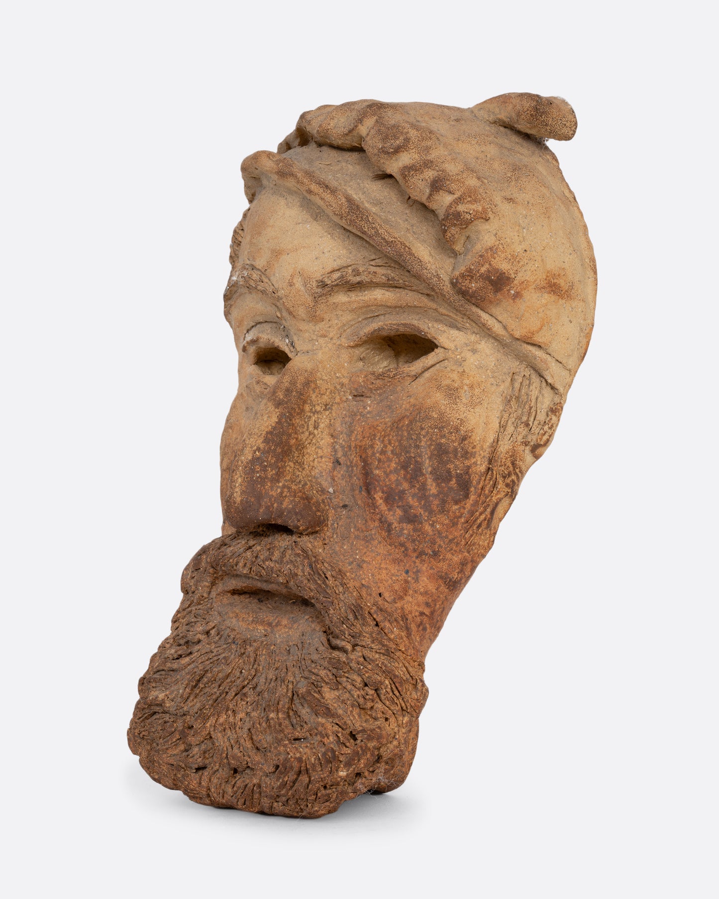 A handmade ceramic mask with a beard and hat. Shown from the side.