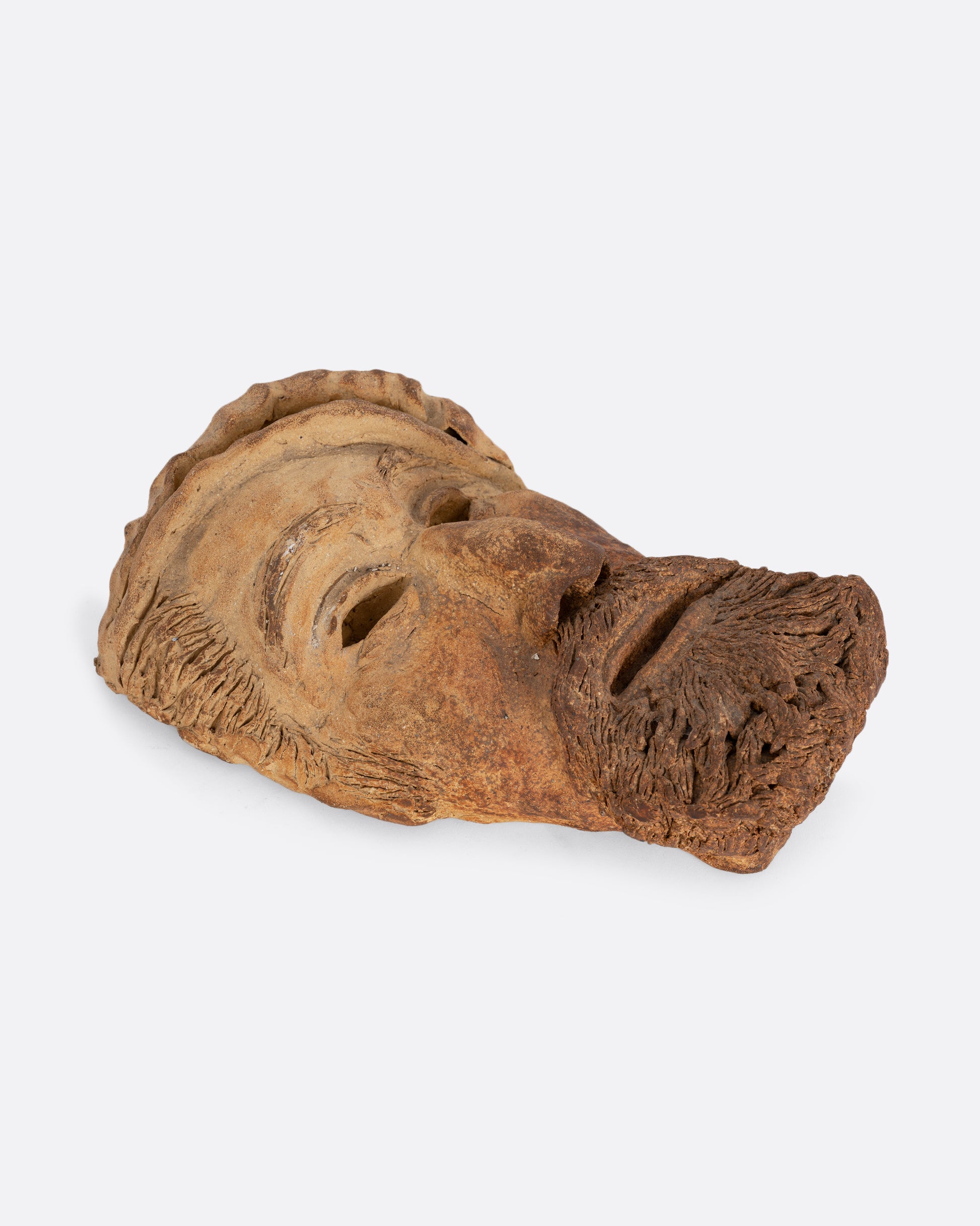 A handmade ceramic mask with a beard and hat. Shown lying flat from the side.